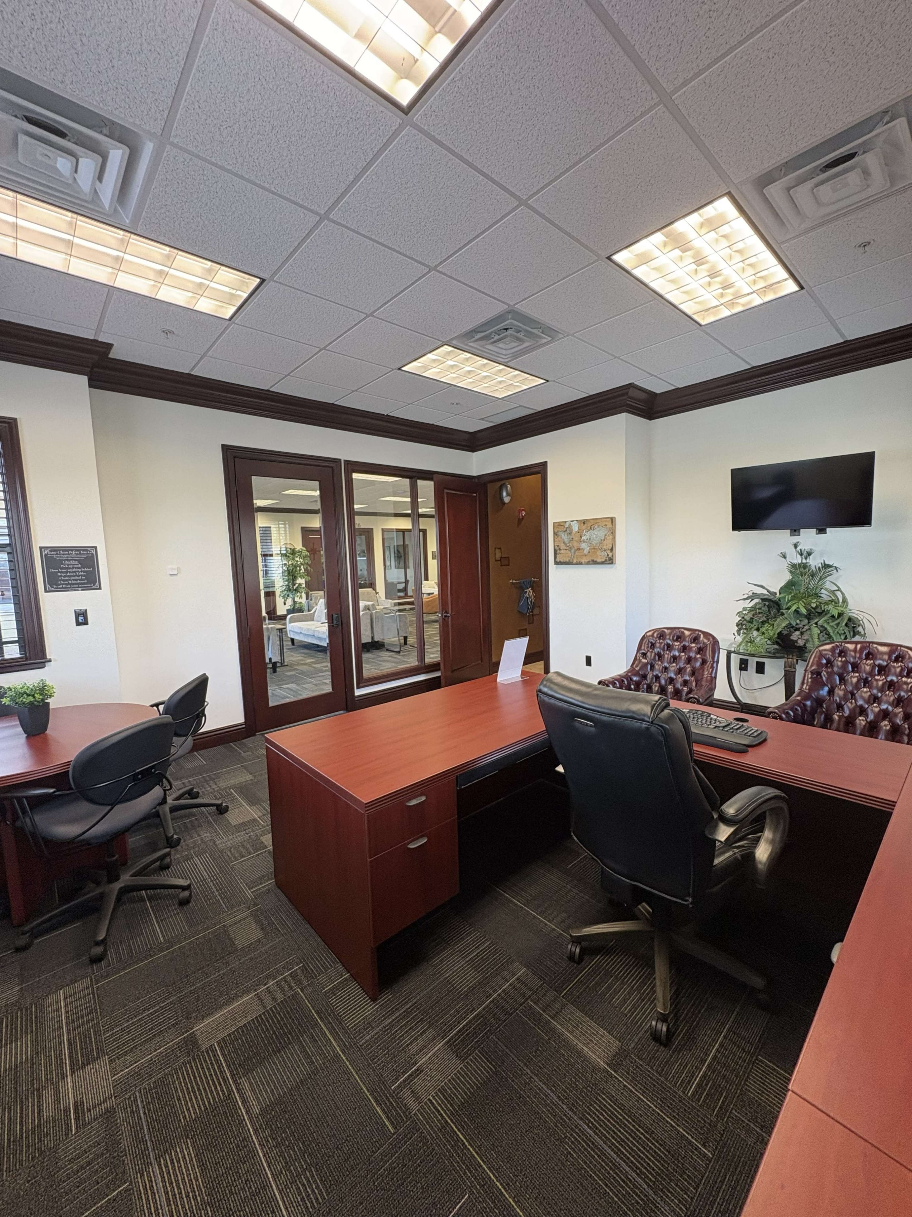 The image shows a modern office space featuring a wooden desk, chairs, and glass doors leading to another room.