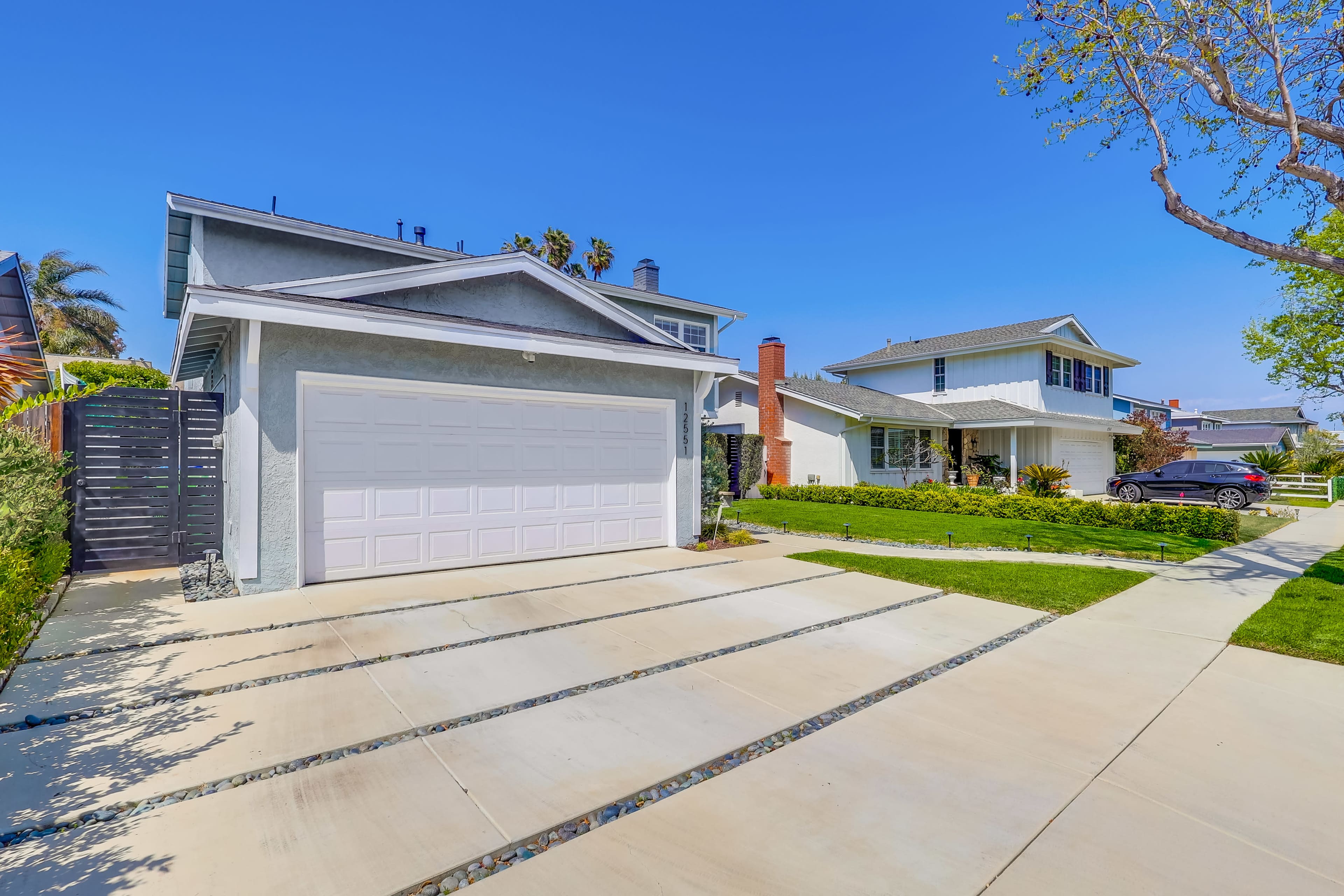 The image shows a suburban neighborhood featuring two houses with a freshly paved driveway and well-maintained lawns.