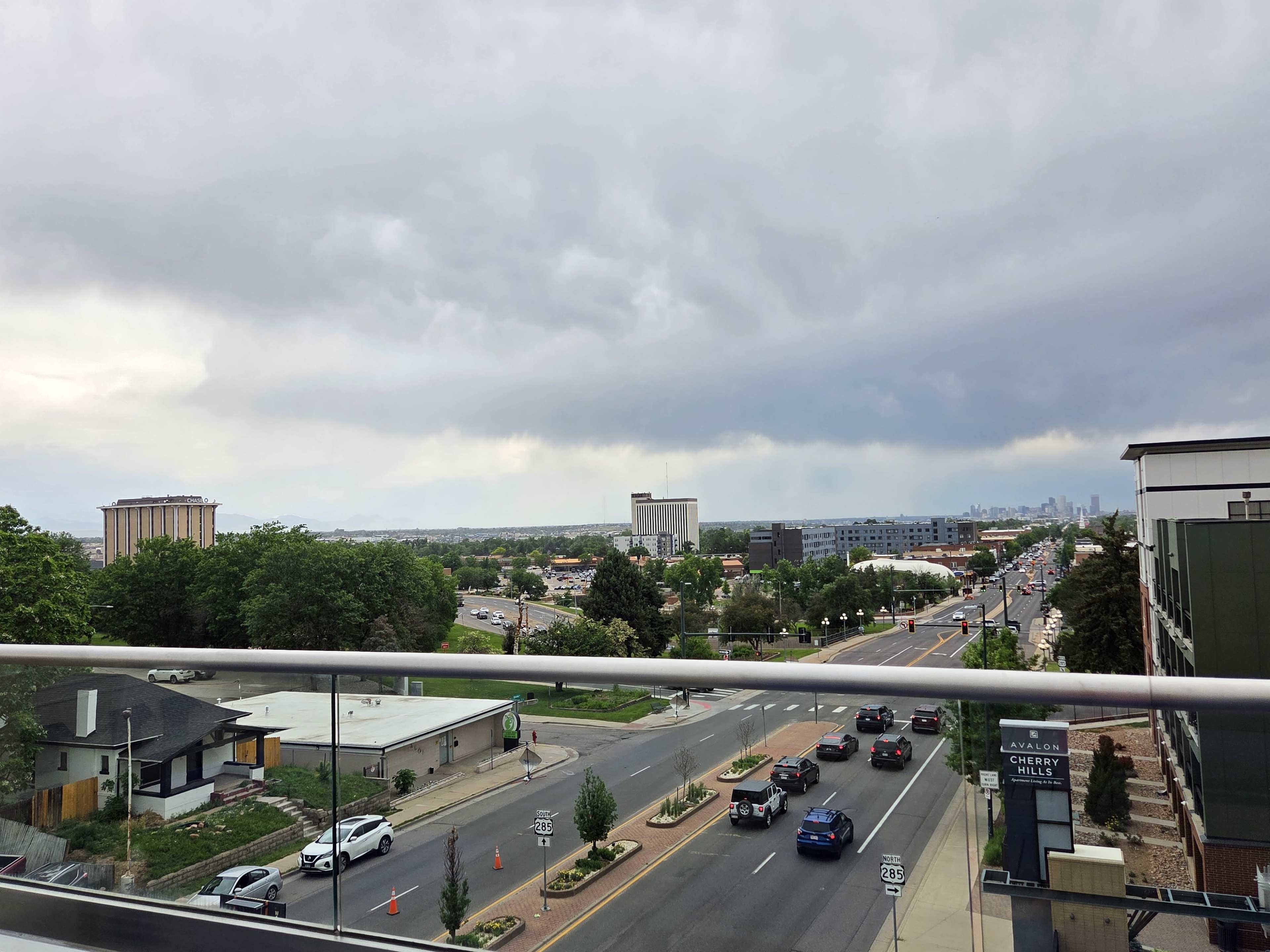 A view of a busy city street lined with trees, buildings, and vehicles, under an overcast sky.