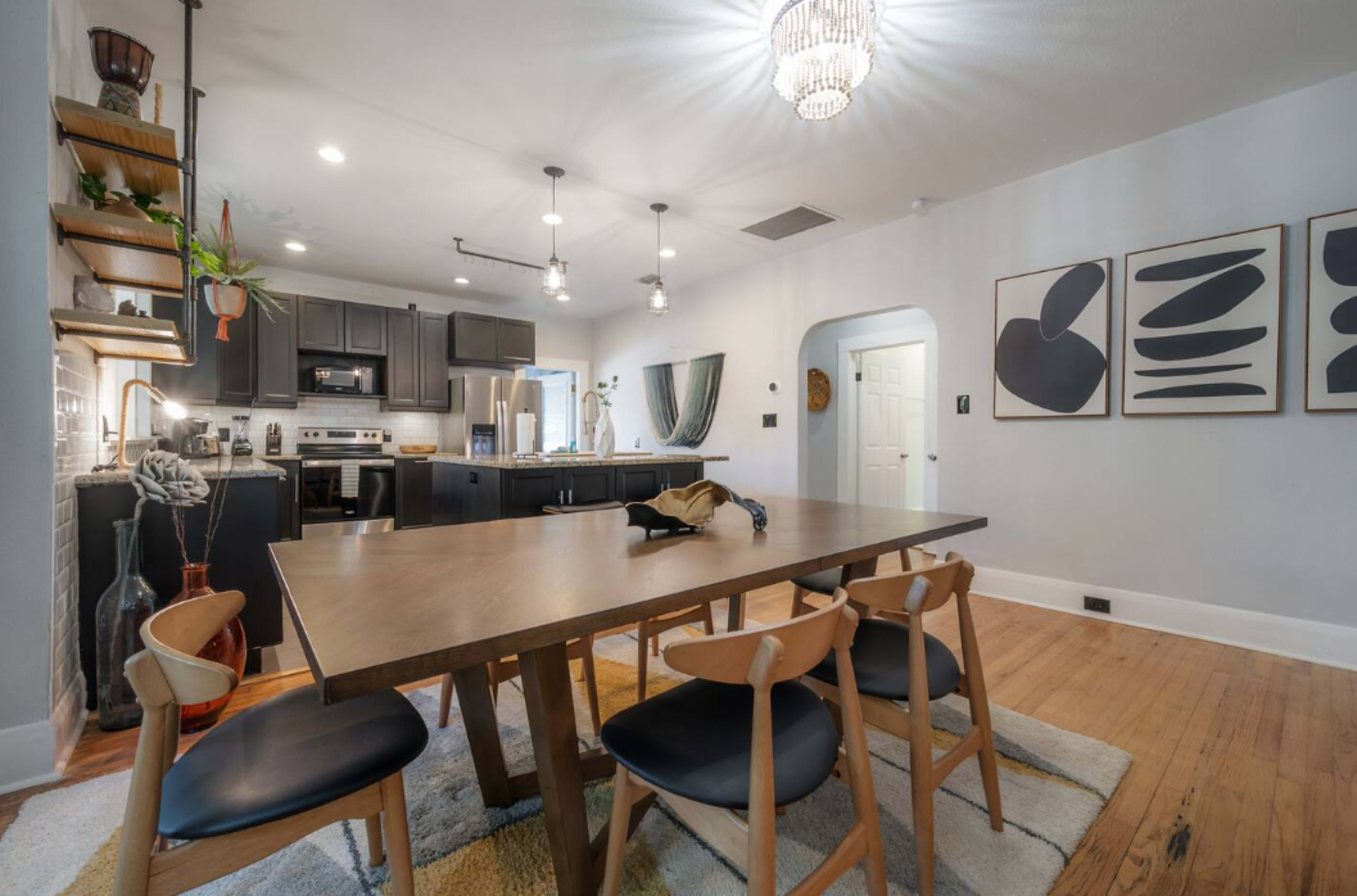 A modern kitchen and dining area with a wooden table surrounded by black chairs, featuring a minimalist design and contemporary decor.