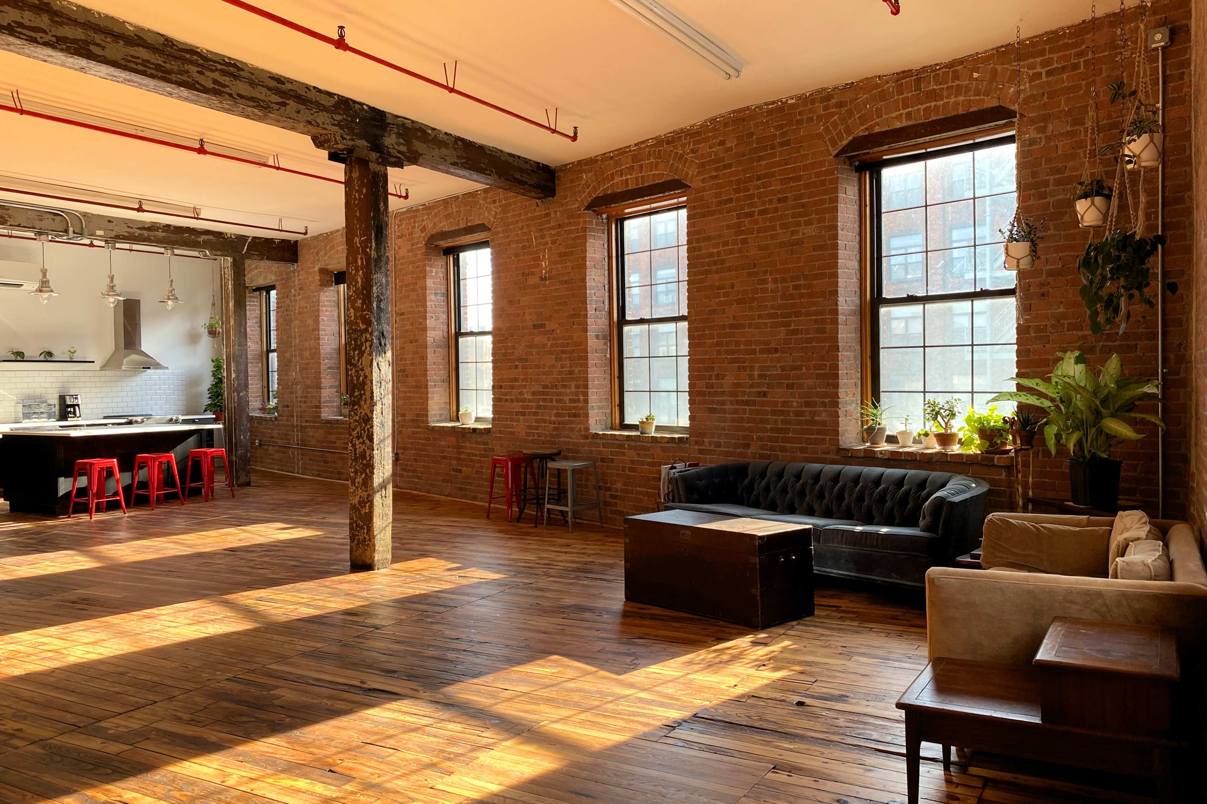 A spacious room with brick walls, large windows, wooden floors, and a mix of modern and vintage furniture arranged throughout.