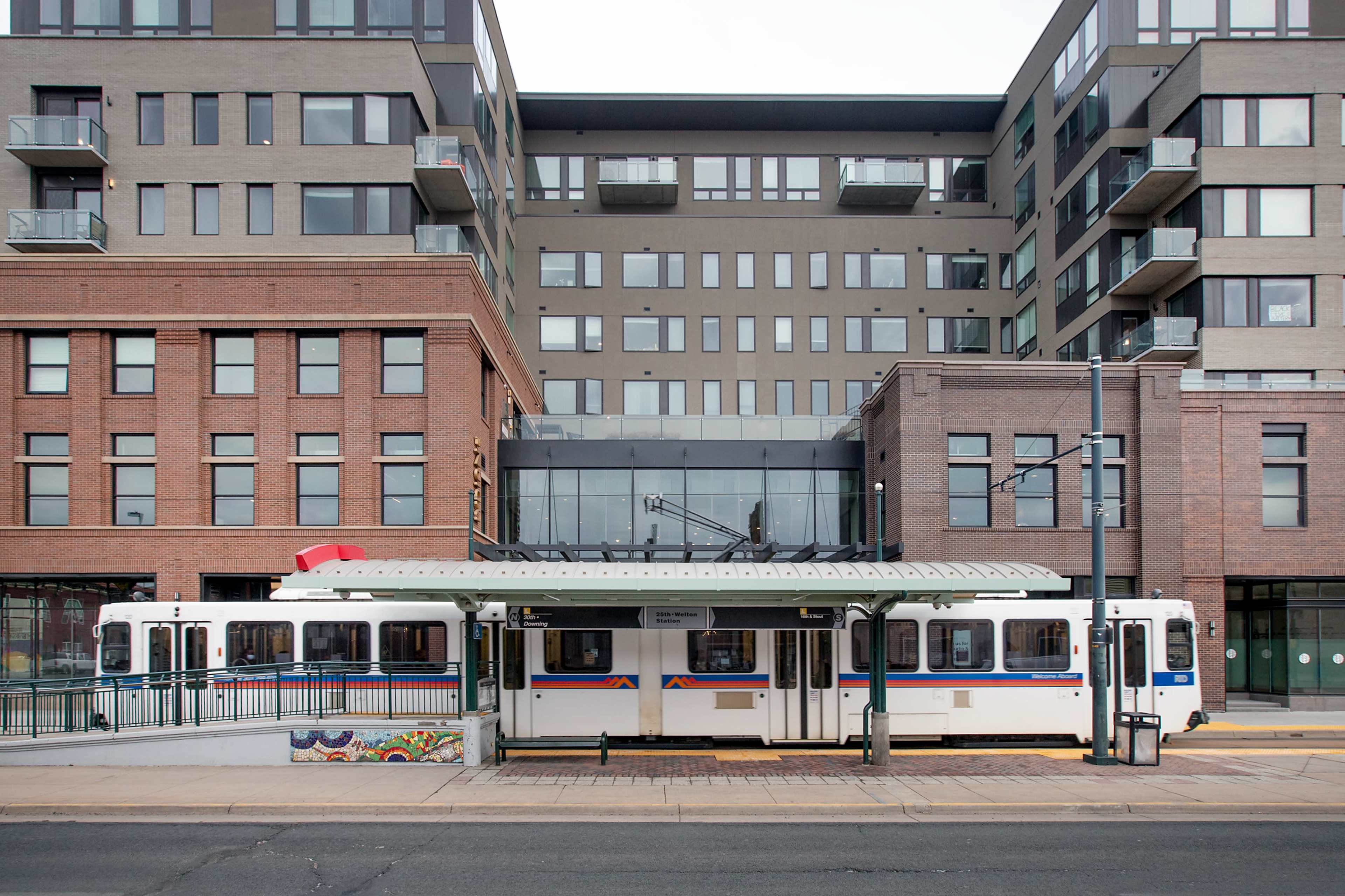 A light rail station is situated in front of a modern multi-story residential building with balconies.