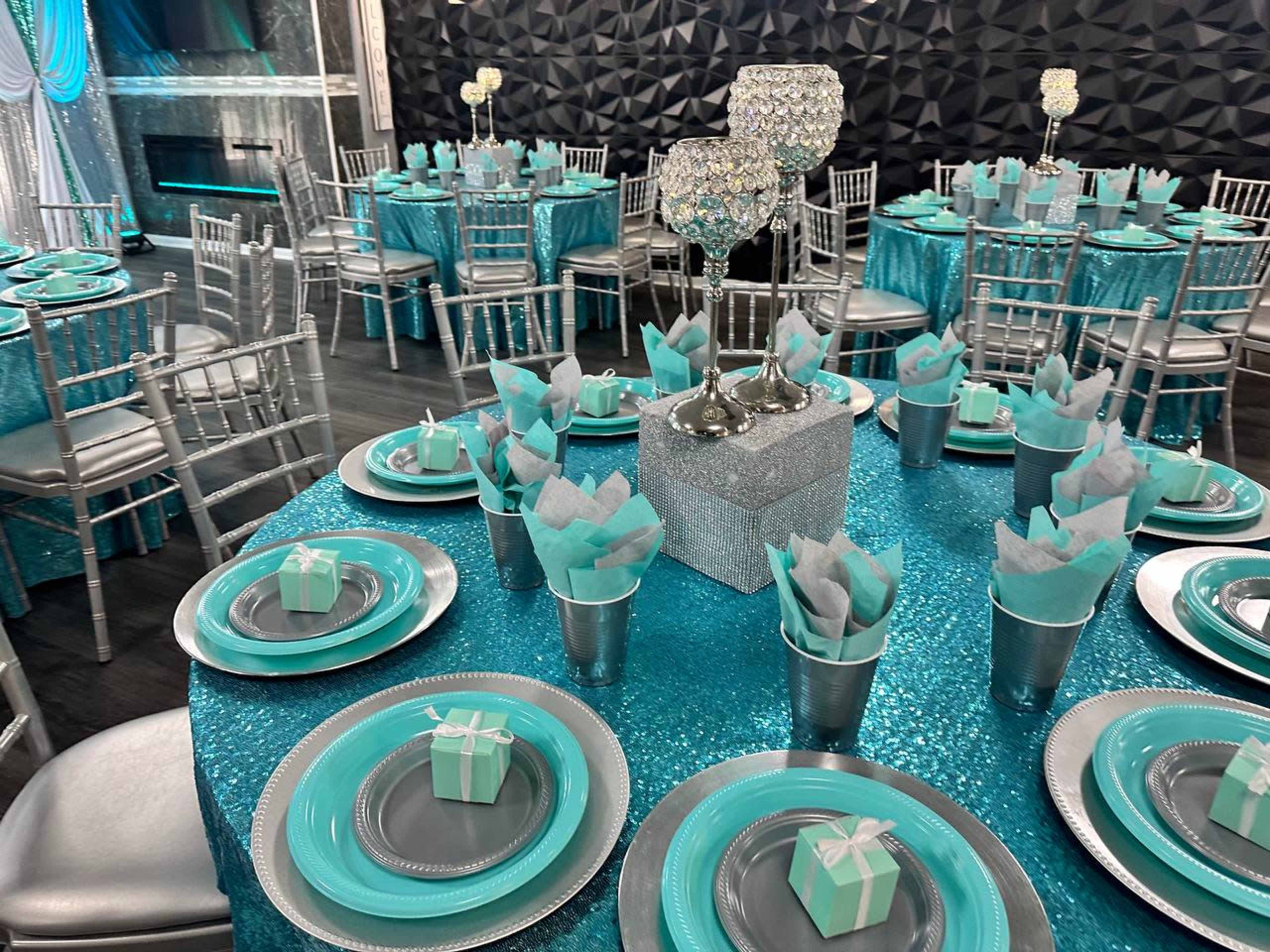 A banquet hall decorated with teal and silver table settings, featuring round tables with sparkling tablecloths and elegantly arranged dishes and centerpieces.