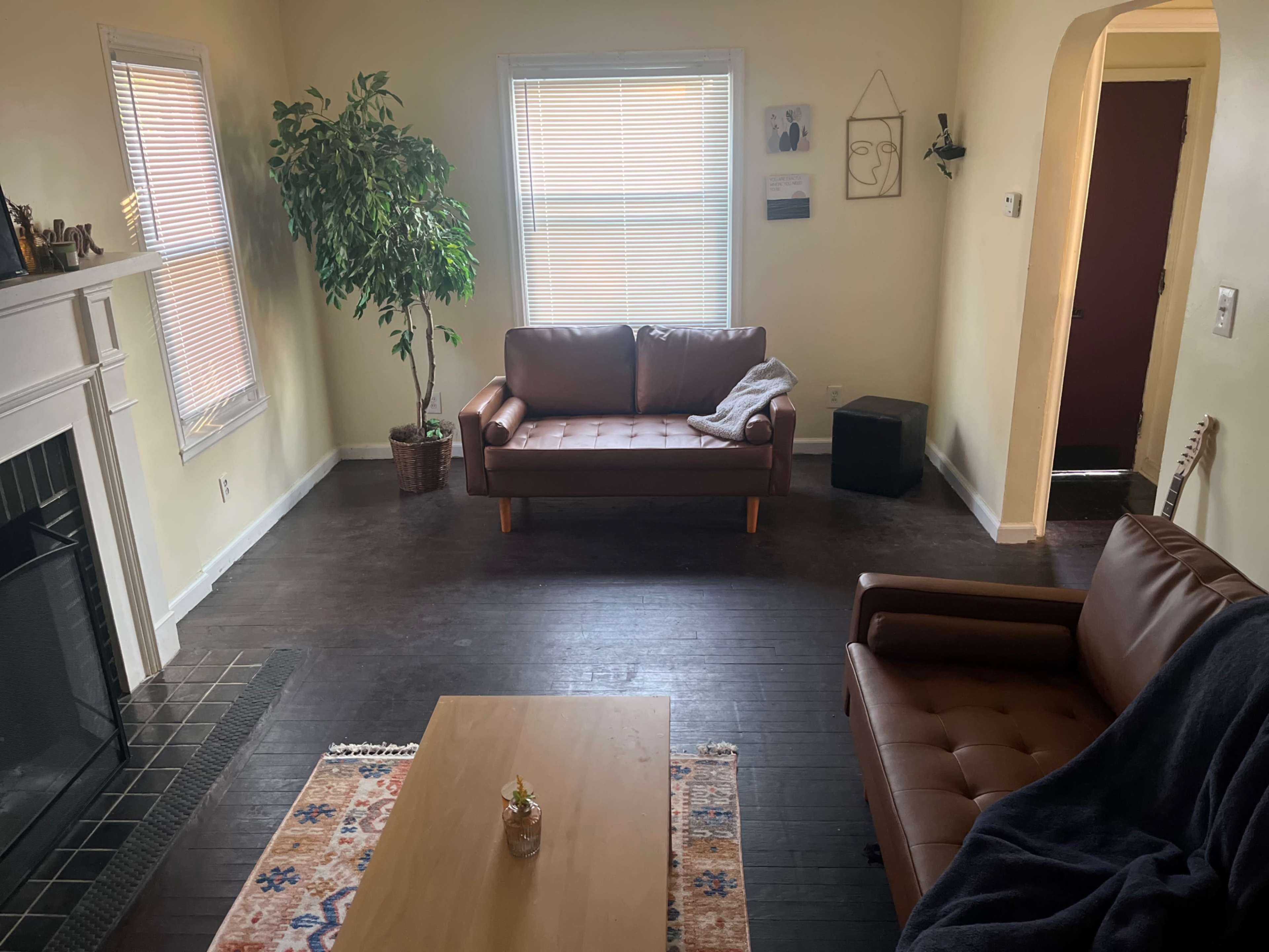 The image shows a living room with two brown sofas, a coffee table, a potted plant, and a doorway leading to another room.