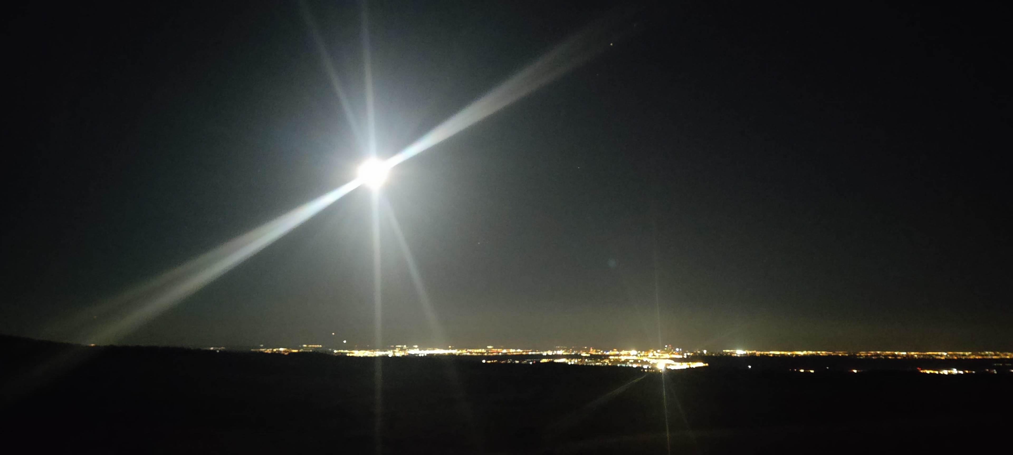 A bright moon illuminates the night sky above a sprawling cityscape, with lights twinkling in the distance.