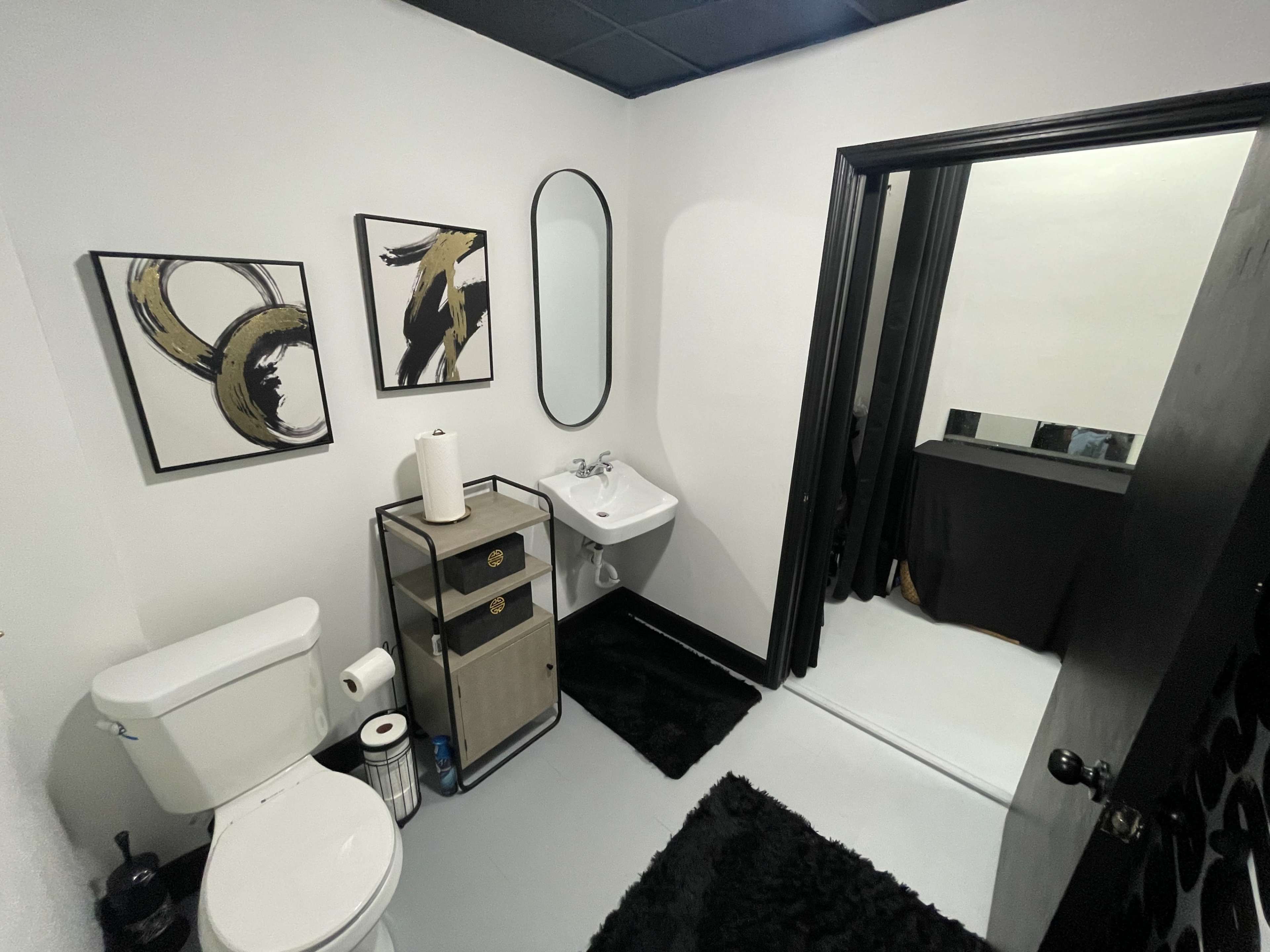 A modern bathroom with a toilet, sink, decorative wall art, and a doorway leading to another room.