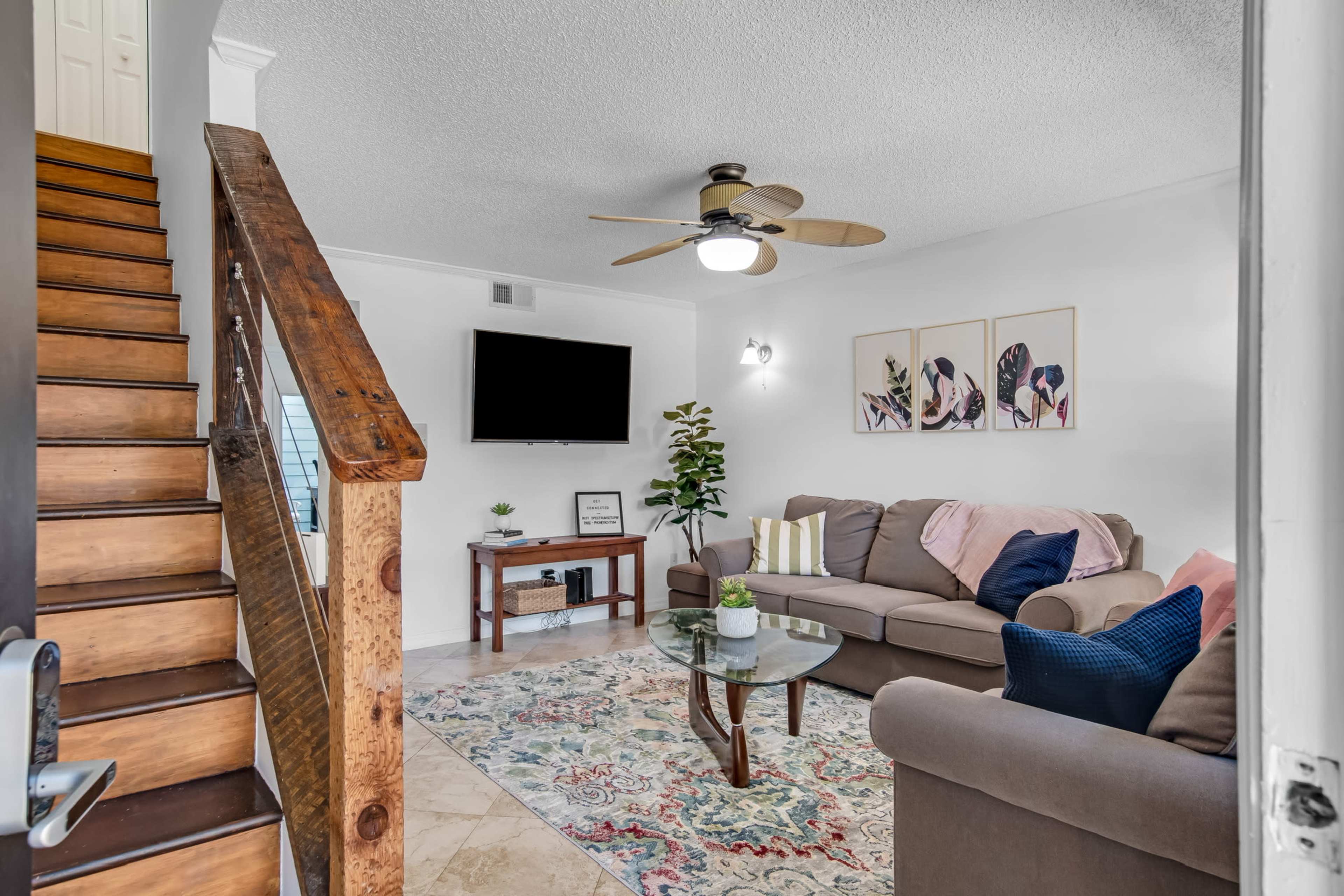 A living room features a sofa, coffee table, and a staircase leading to another level, with a wall-mounted TV and decorative wall art.
