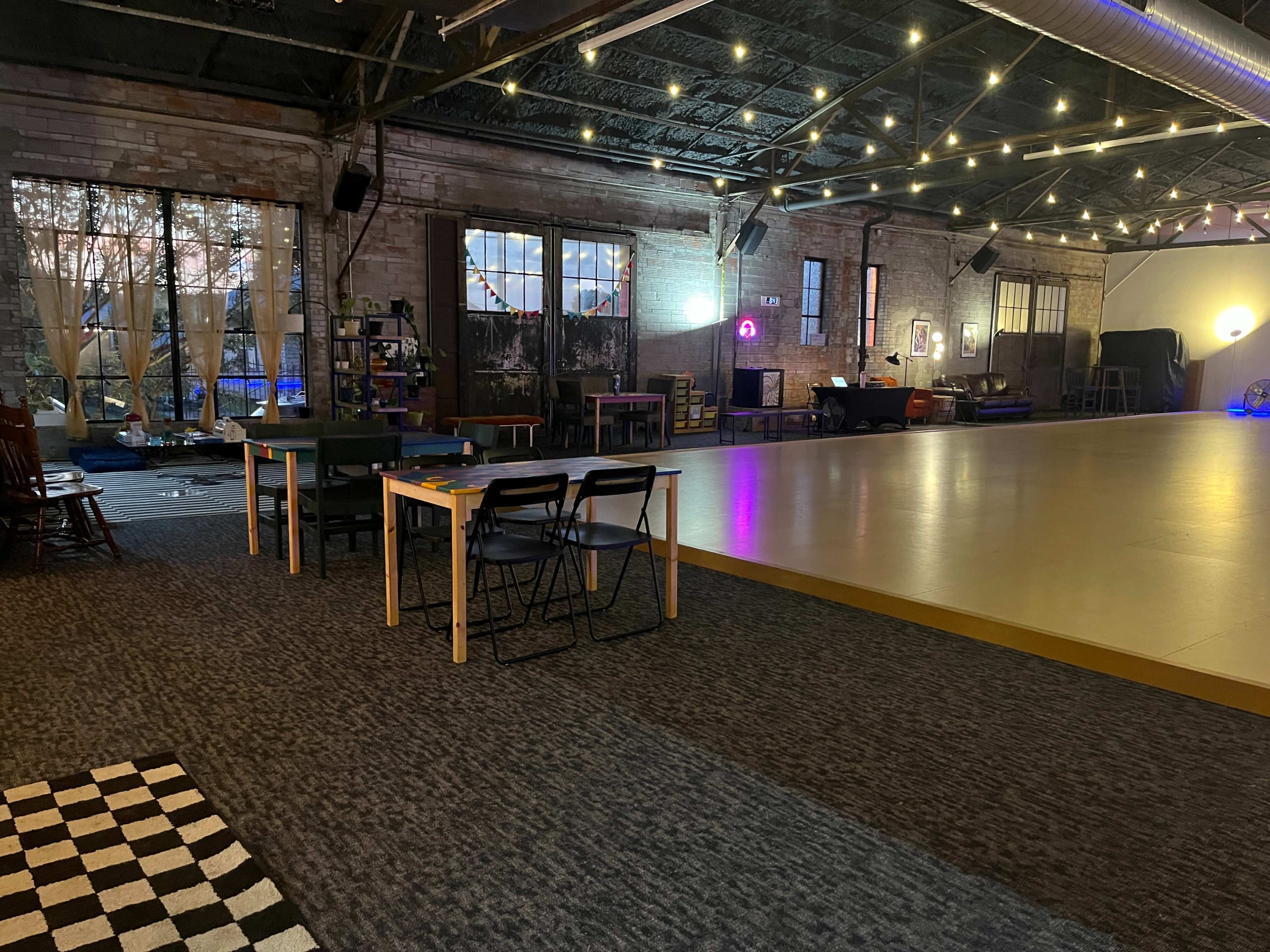 The image shows a spacious indoor area with polished flooring, several tables and chairs, and large windows that allow natural light to enter, creating a cozy atmosphere.
