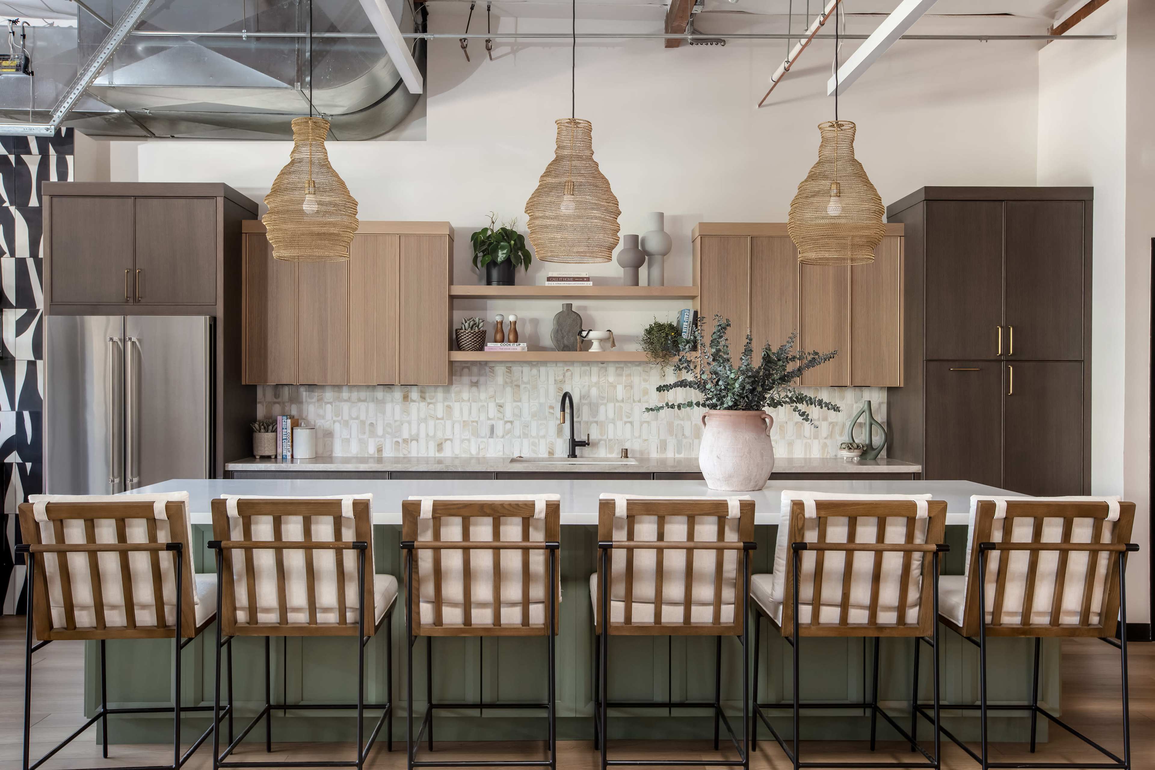 A modern kitchen features a large island with eight stools, woven pendant lights, and cabinetry in neutral tones.