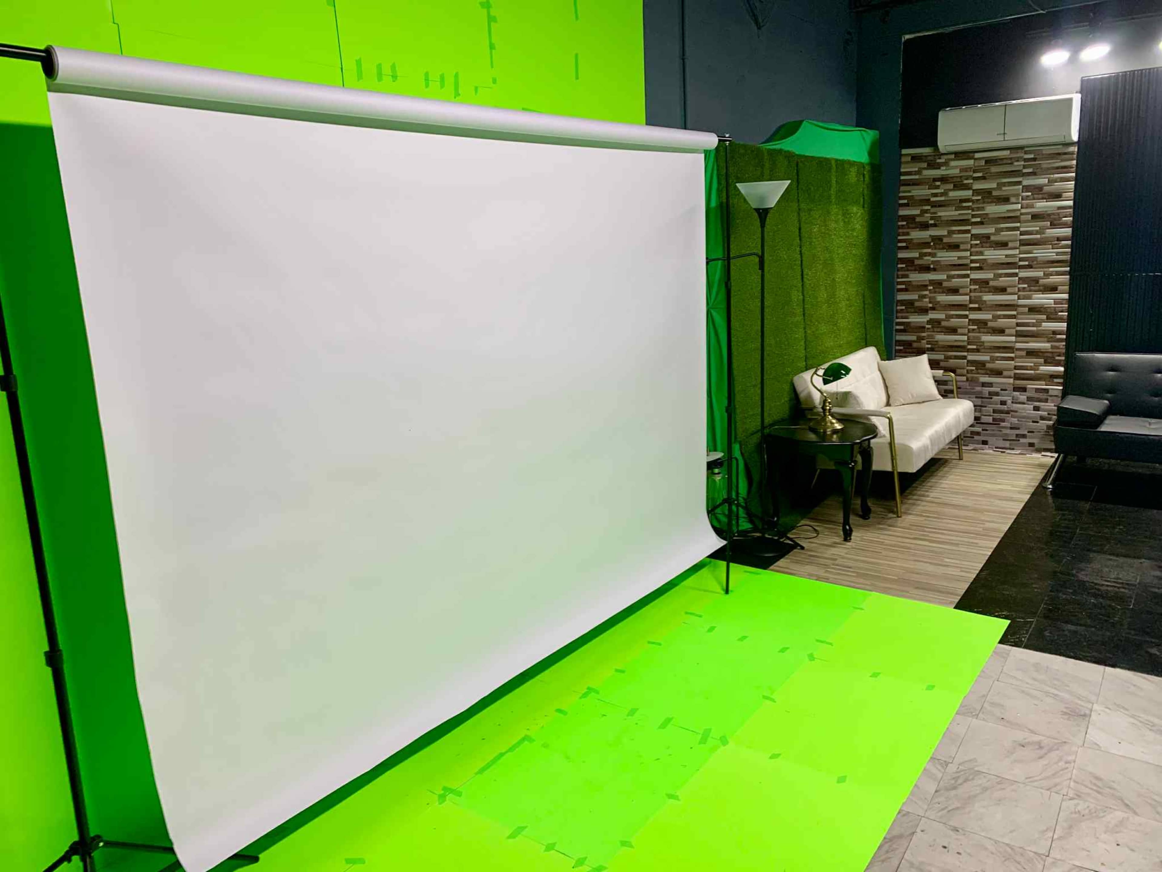 The image shows a photography studio equipped with a green screen backdrop and a light-colored sofa set against a textured wall.