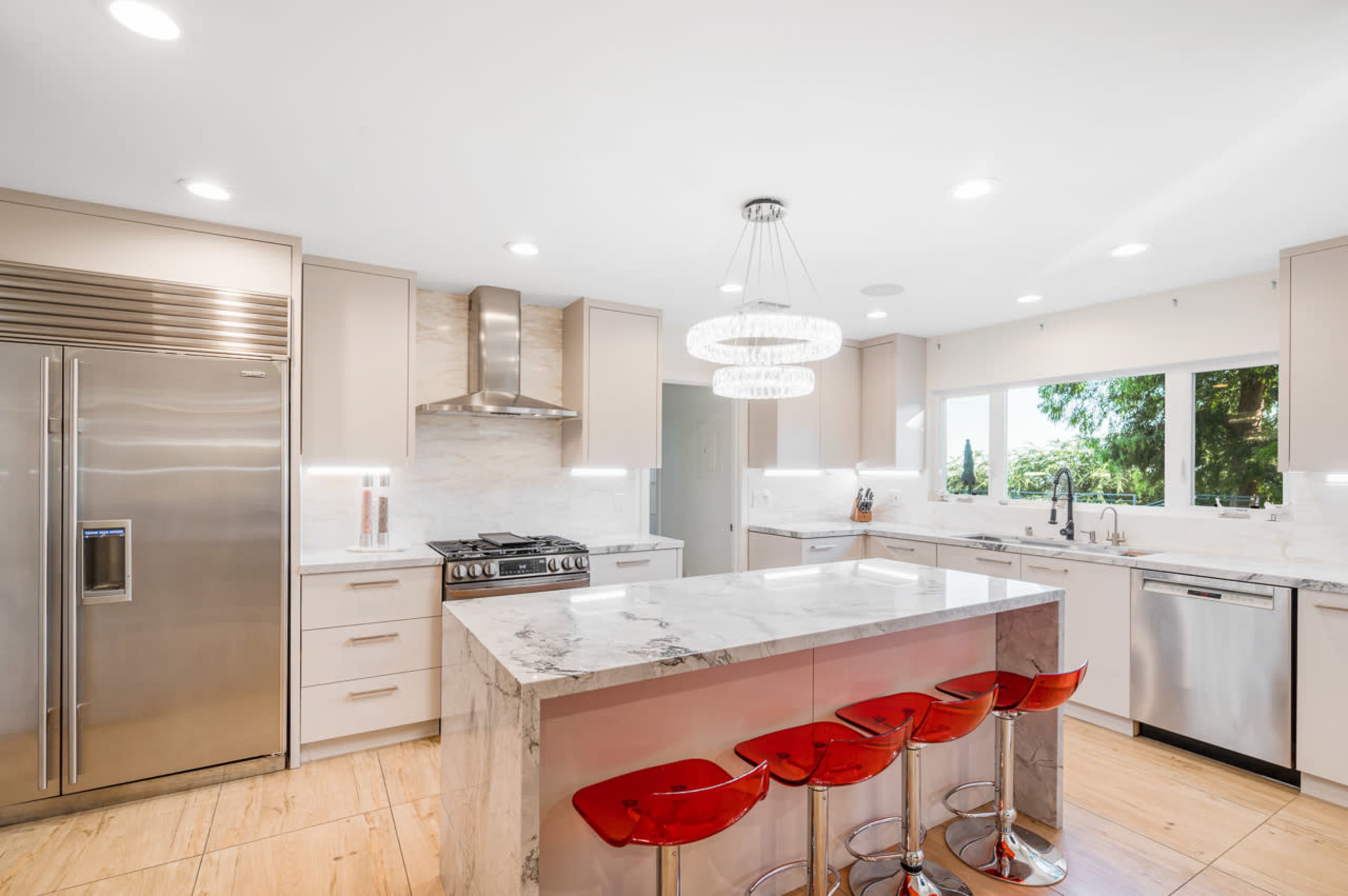 The kitchen features modern appliances, a large marble island, and red bar stools.