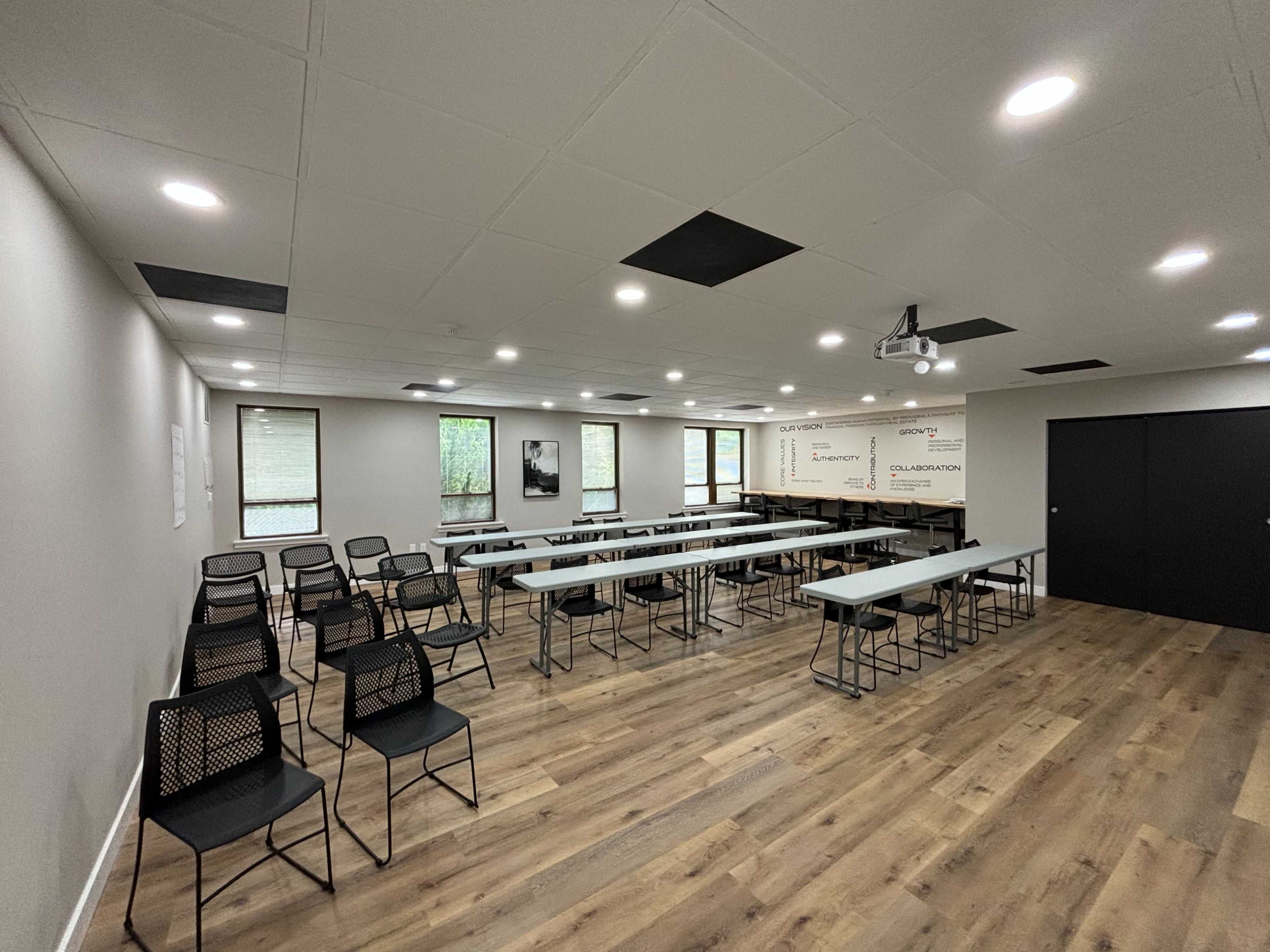 A conference room set up with rows of chairs facing long tables, equipped with modern lighting and a projector.