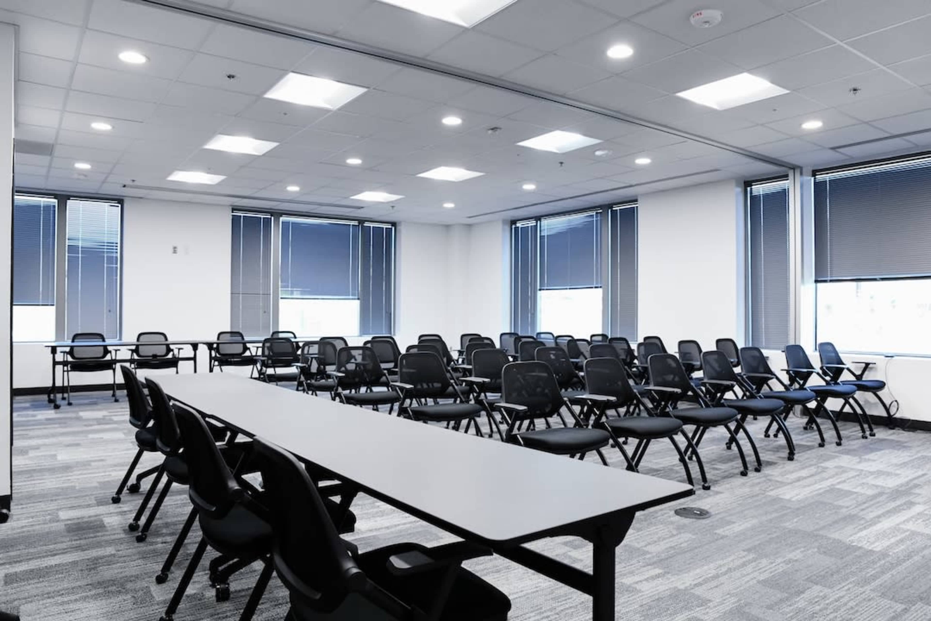 The image shows a modern conference room with rows of chairs and tables set up for a meeting or presentation.