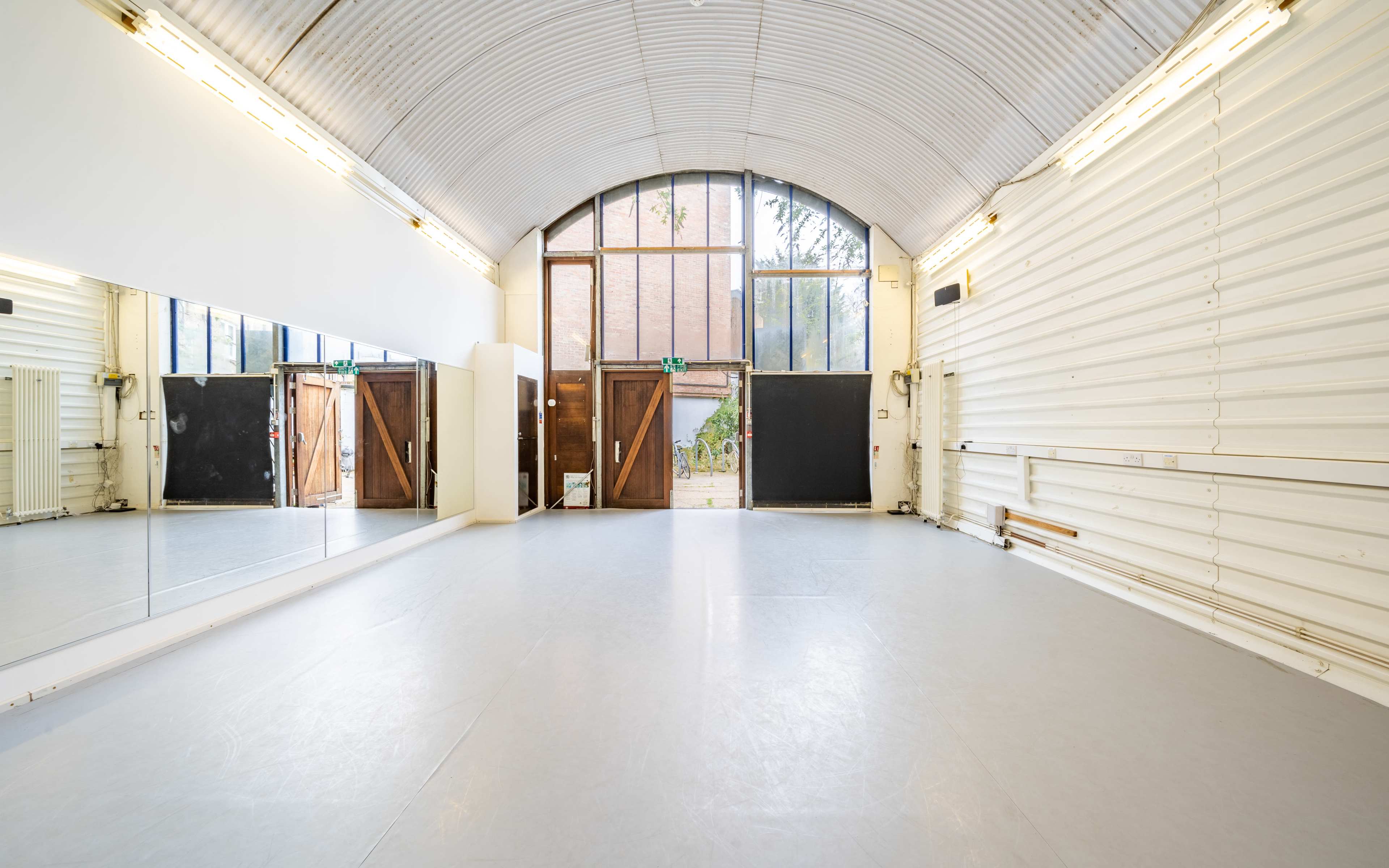 A spacious dance studio with mirrored walls, large windows, and a light gray floor.
