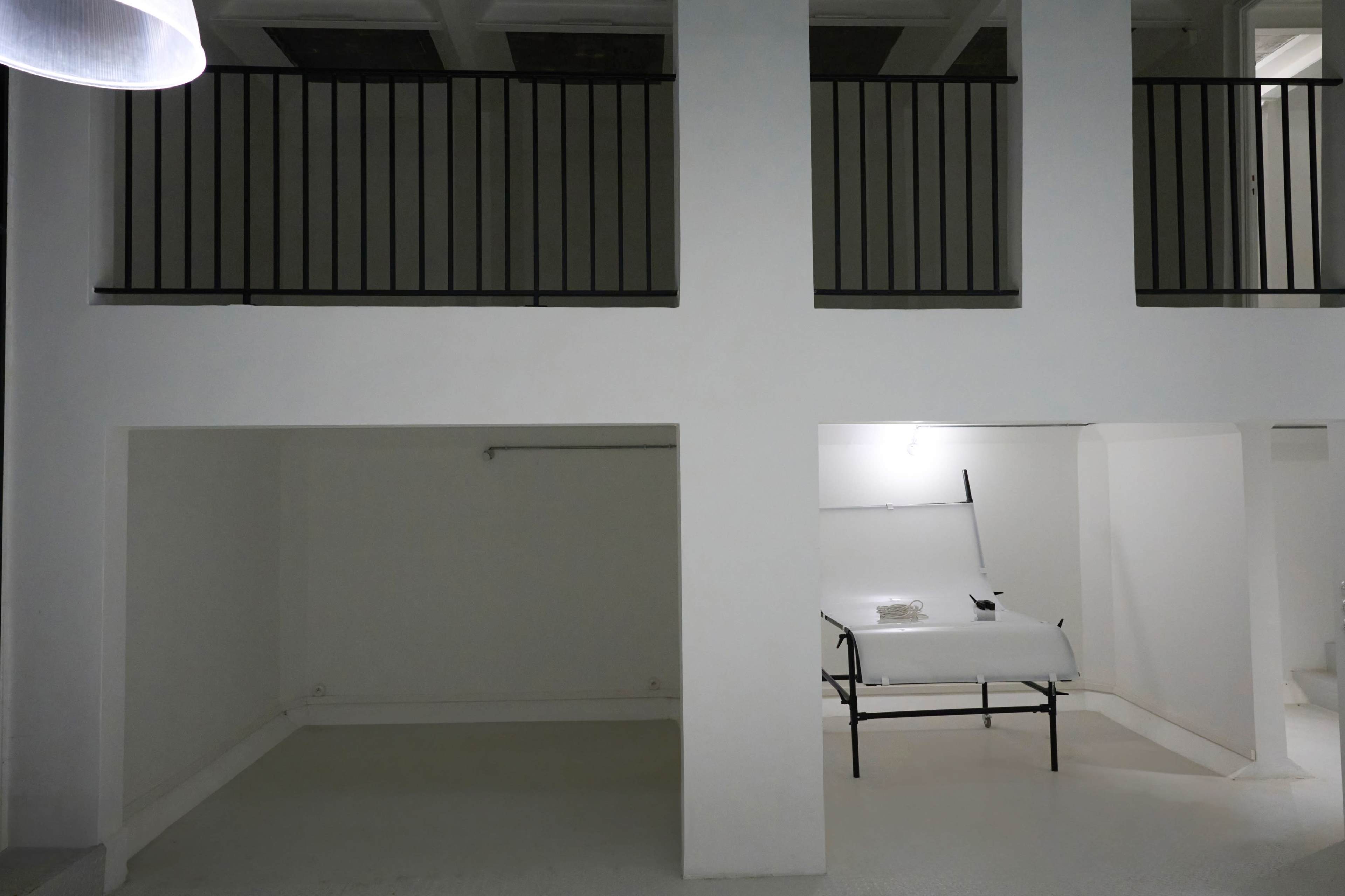 A minimalist interior space with a black railing on the upper floor and a folding table positioned under a soft overhead light.