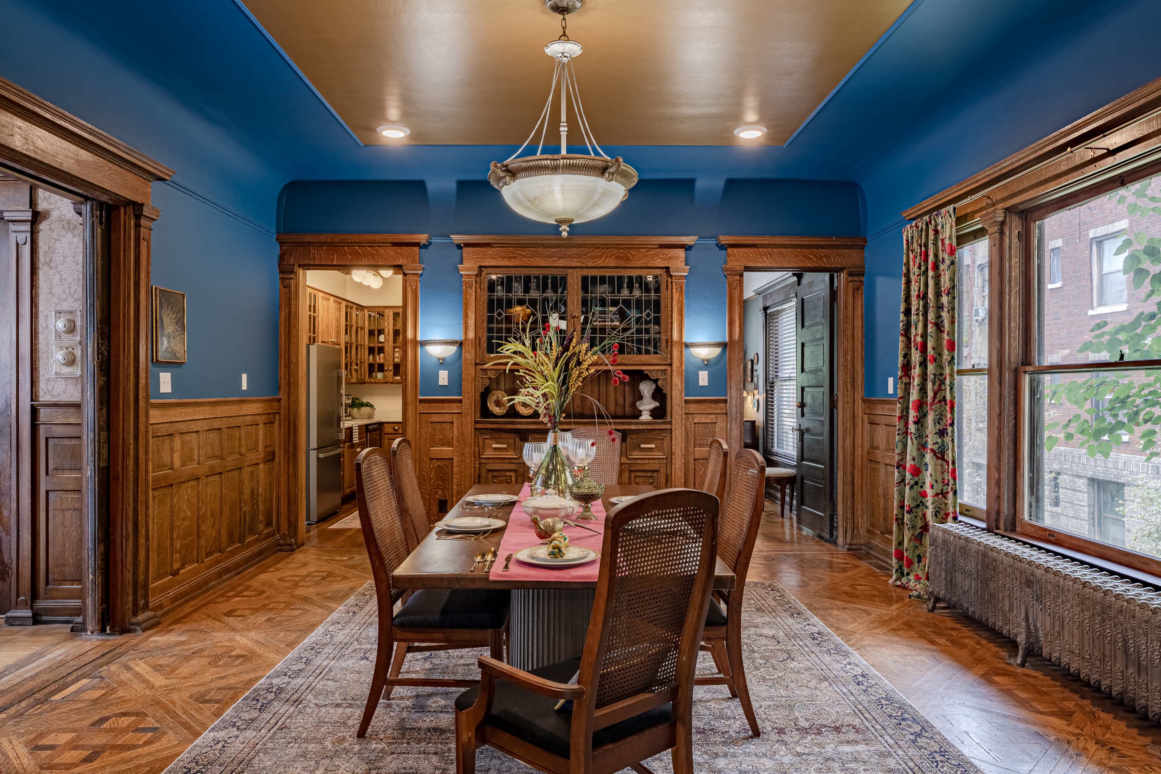 A dining room with a wooden table set for a meal, surrounded by chairs, and features blue walls and decorative window curtains.