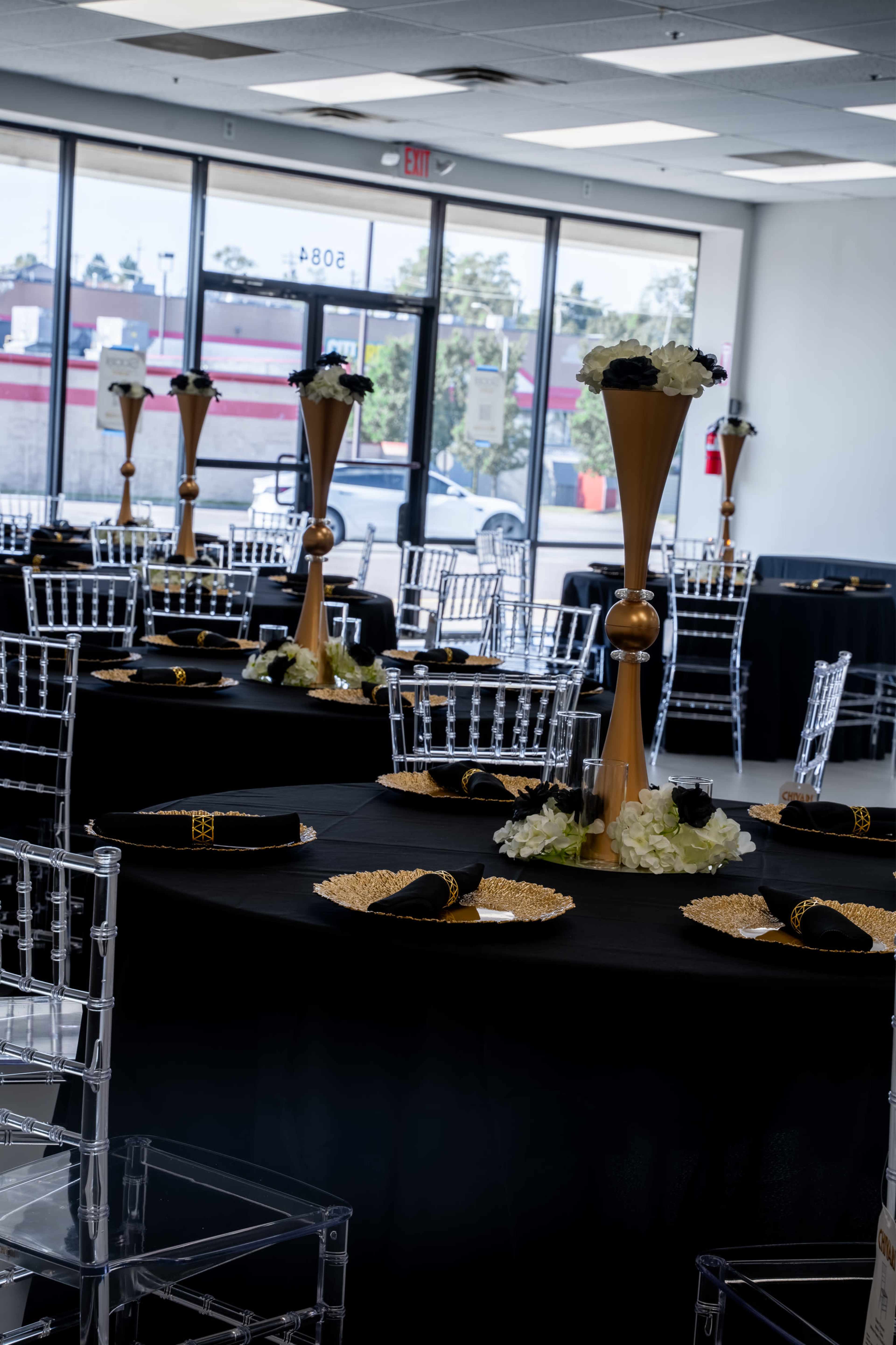 The image shows a banquet hall set up with elegant tables adorned with black tablecloths, tall centerpieces, and decorative plates.