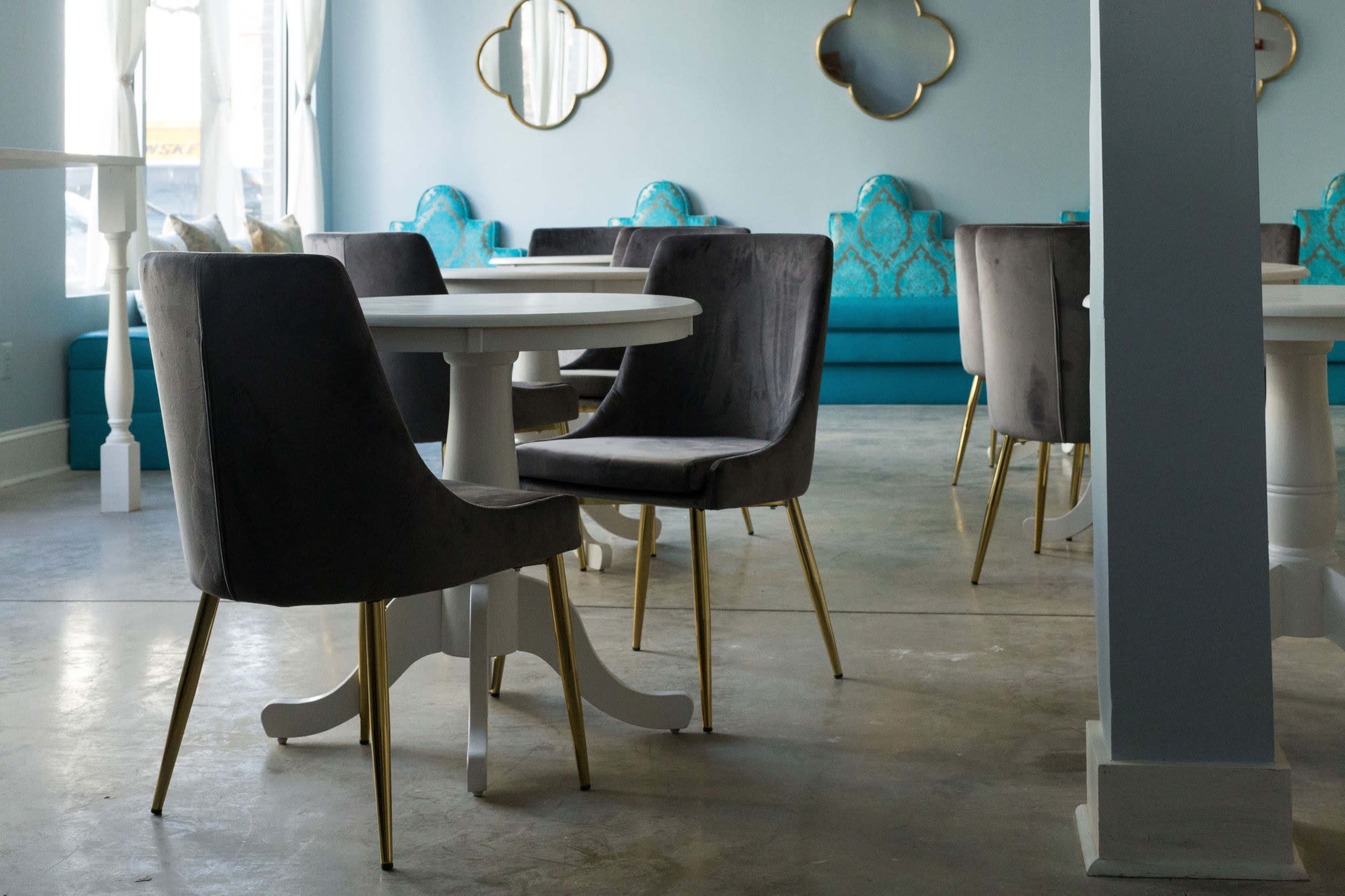 The image shows a modern dining area with white tables, gray chairs with gold legs, and turquoise upholstered seating along the walls.