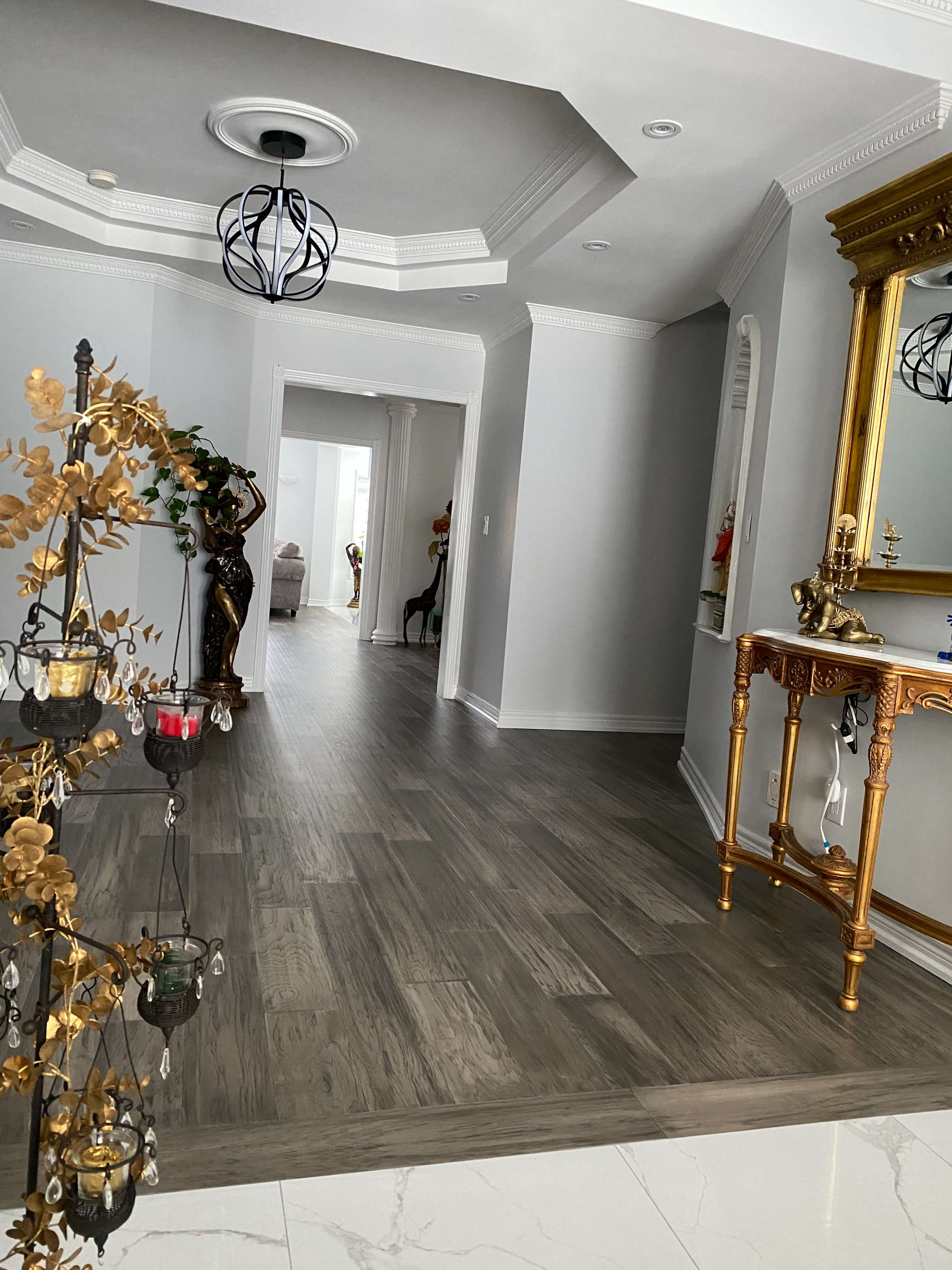 A well-decorated hallway with a decorative golden console table and a stylized light fixture, leading to a larger room in the background.