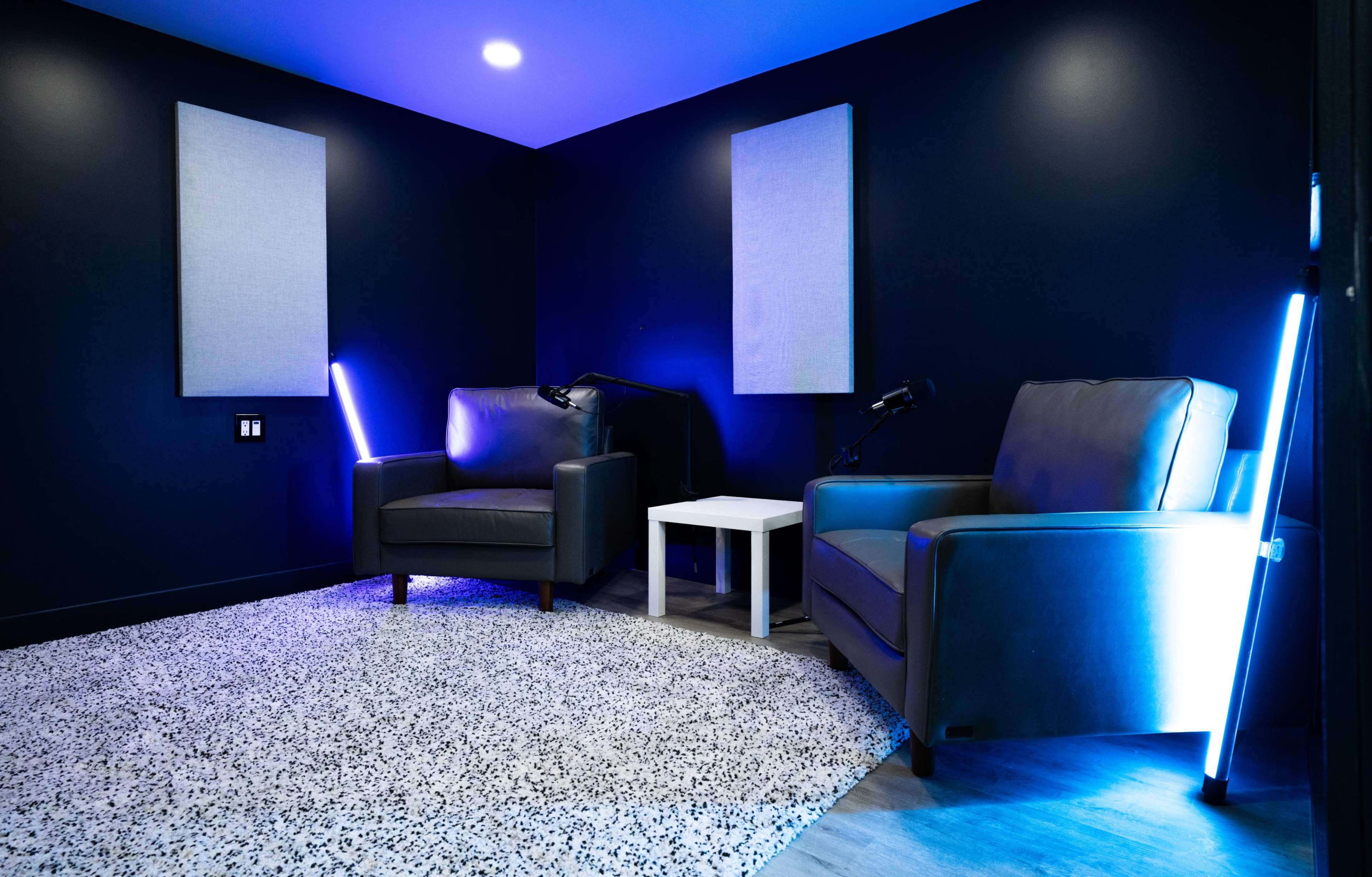 A dimly lit room with two armchairs, a small white table, and blue LED lighting against black walls.