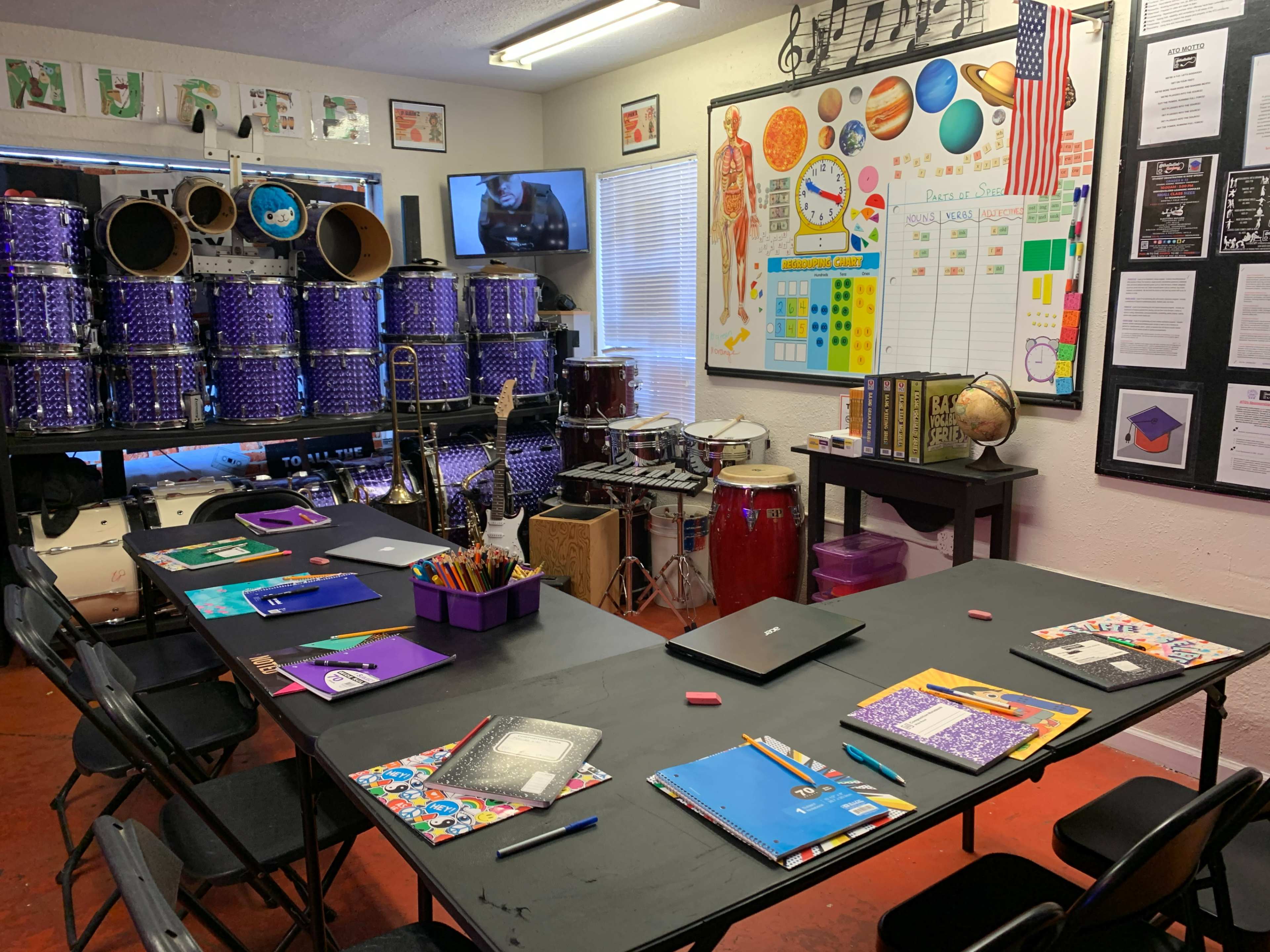 A classroom is arranged with a black table, chairs, and educational materials, featuring musical instruments and a variety of charts on the walls.