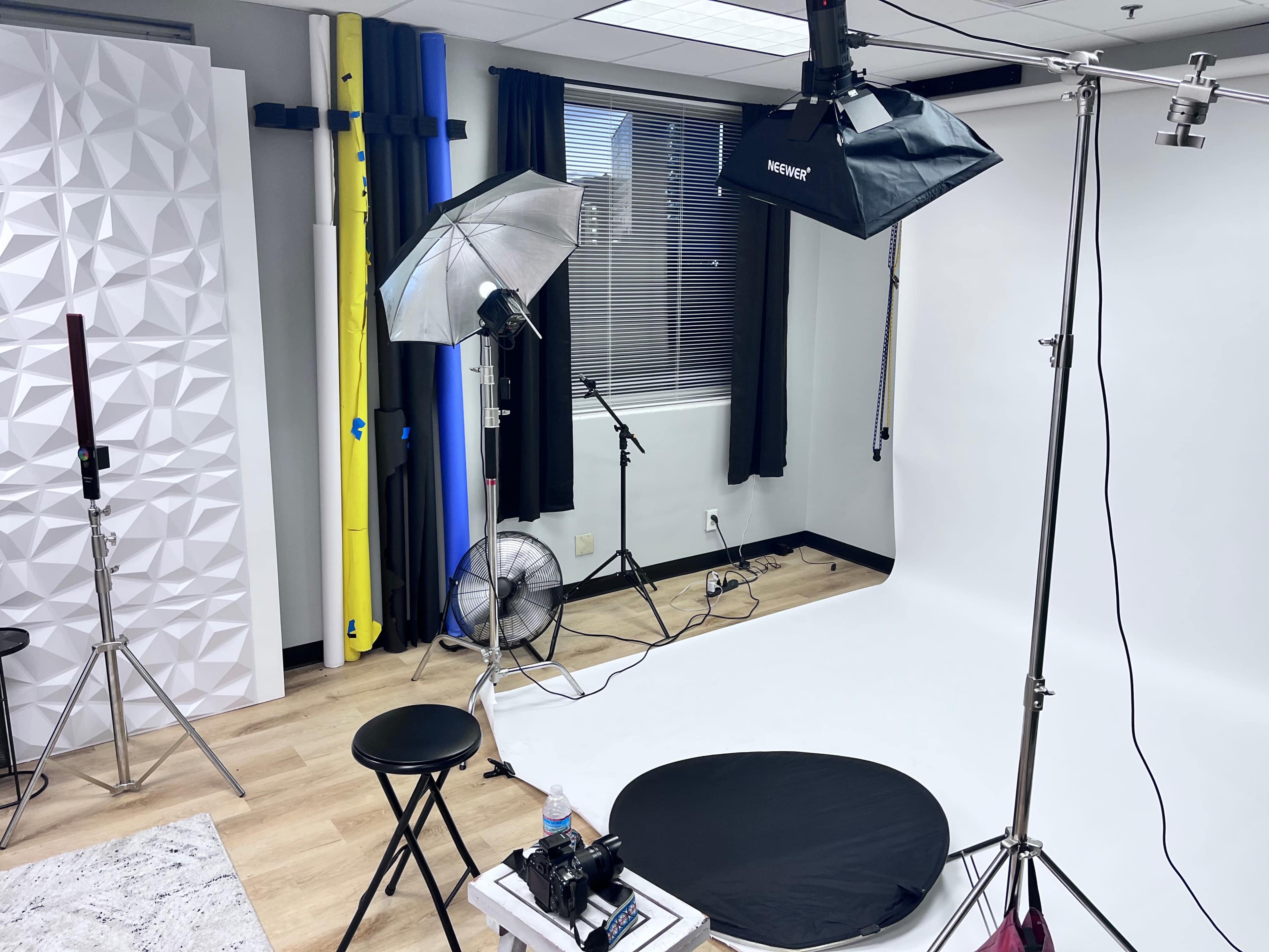 A photography studio equipped with lighting equipment, a black backdrop, a stool, and a white background.