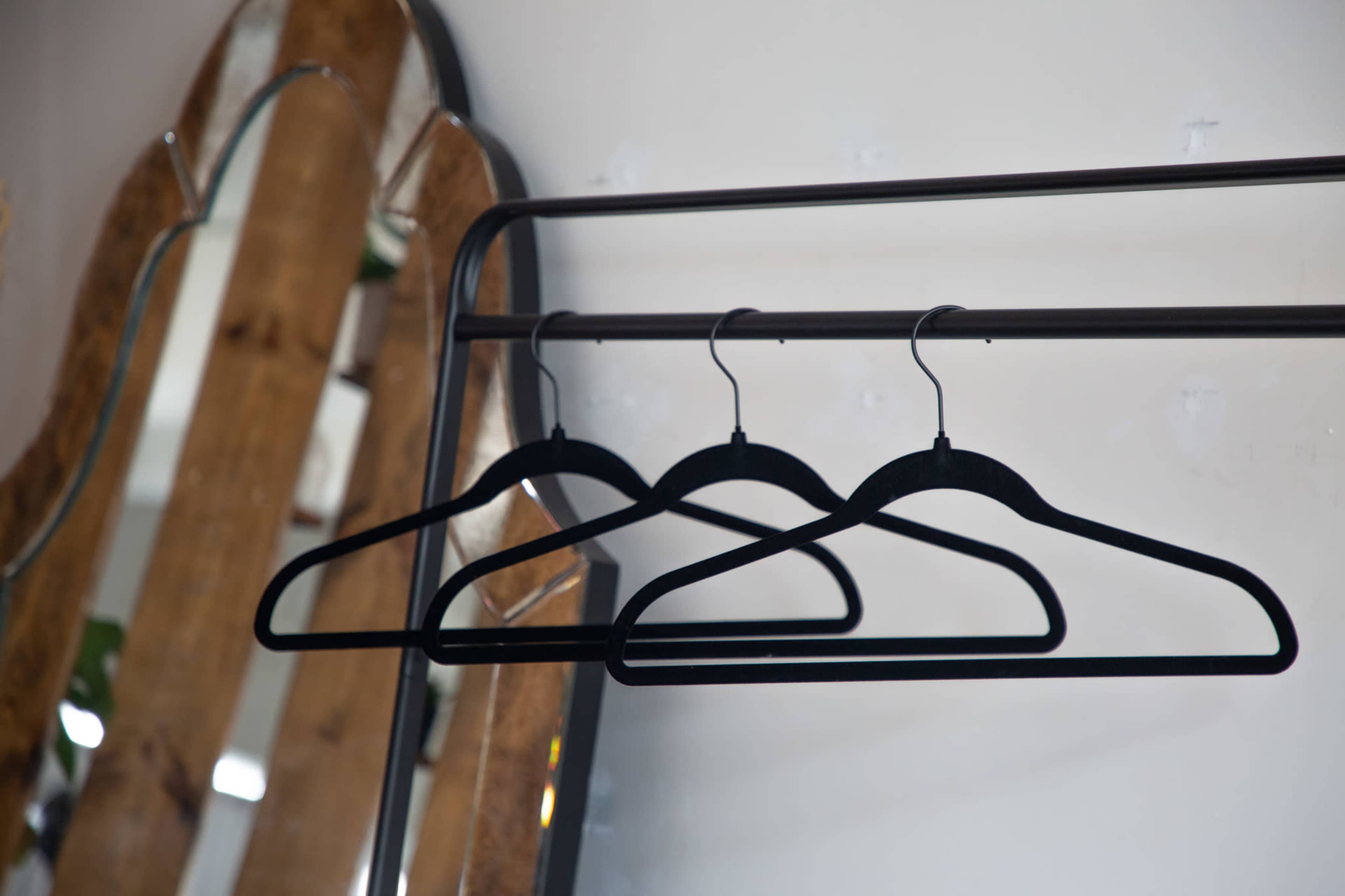 Three black clothing hangers are suspended on a metal rack in front of a wooden-framed mirror.