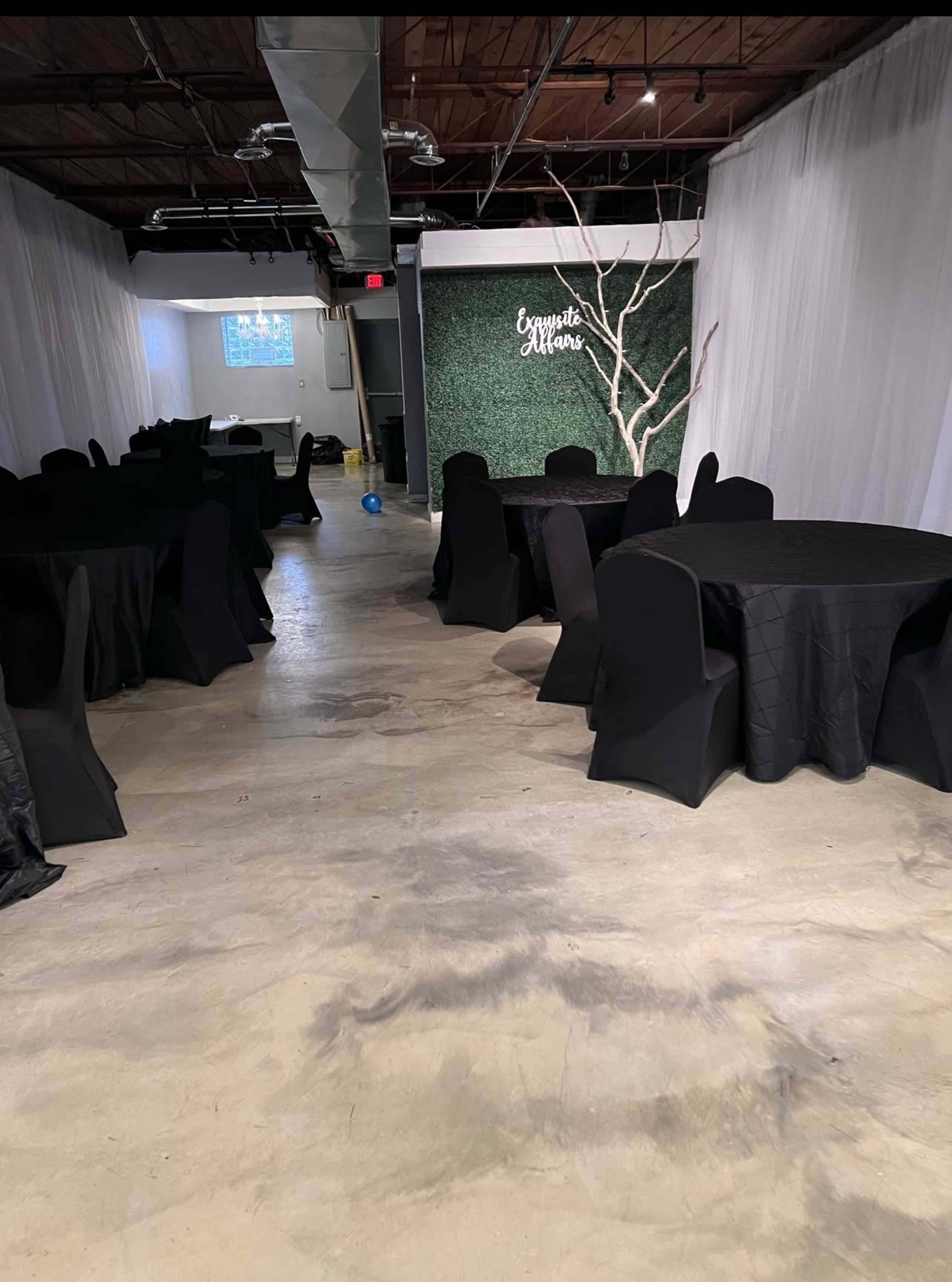 A banquet hall with black tablecloths, chairs, and a decorative wall featuring a white tree branch and text that reads "Ceremony Attire".