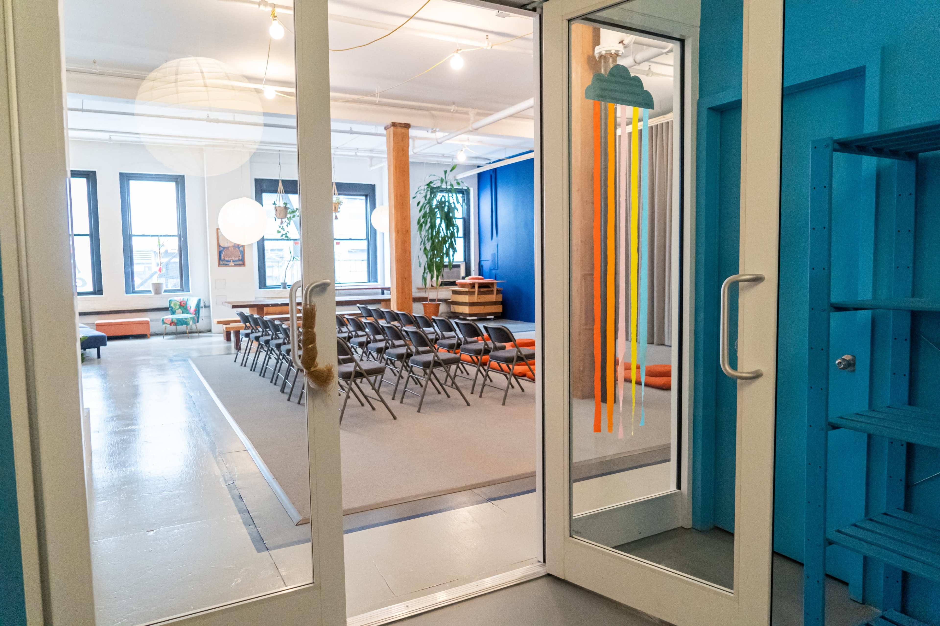 A view through glass double doors into a brightly colored room set up with rows of chairs and decorative elements.