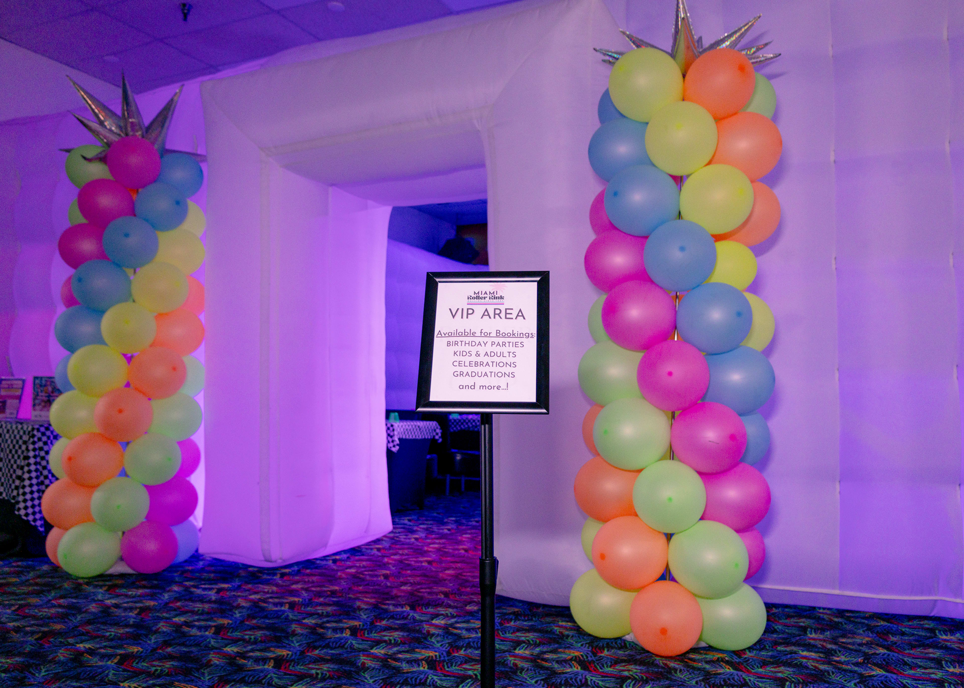 The image features an entrance archway made of colorful balloons labeled as a "VIP AREA," set against a backdrop of a venue with a decorated floor.
