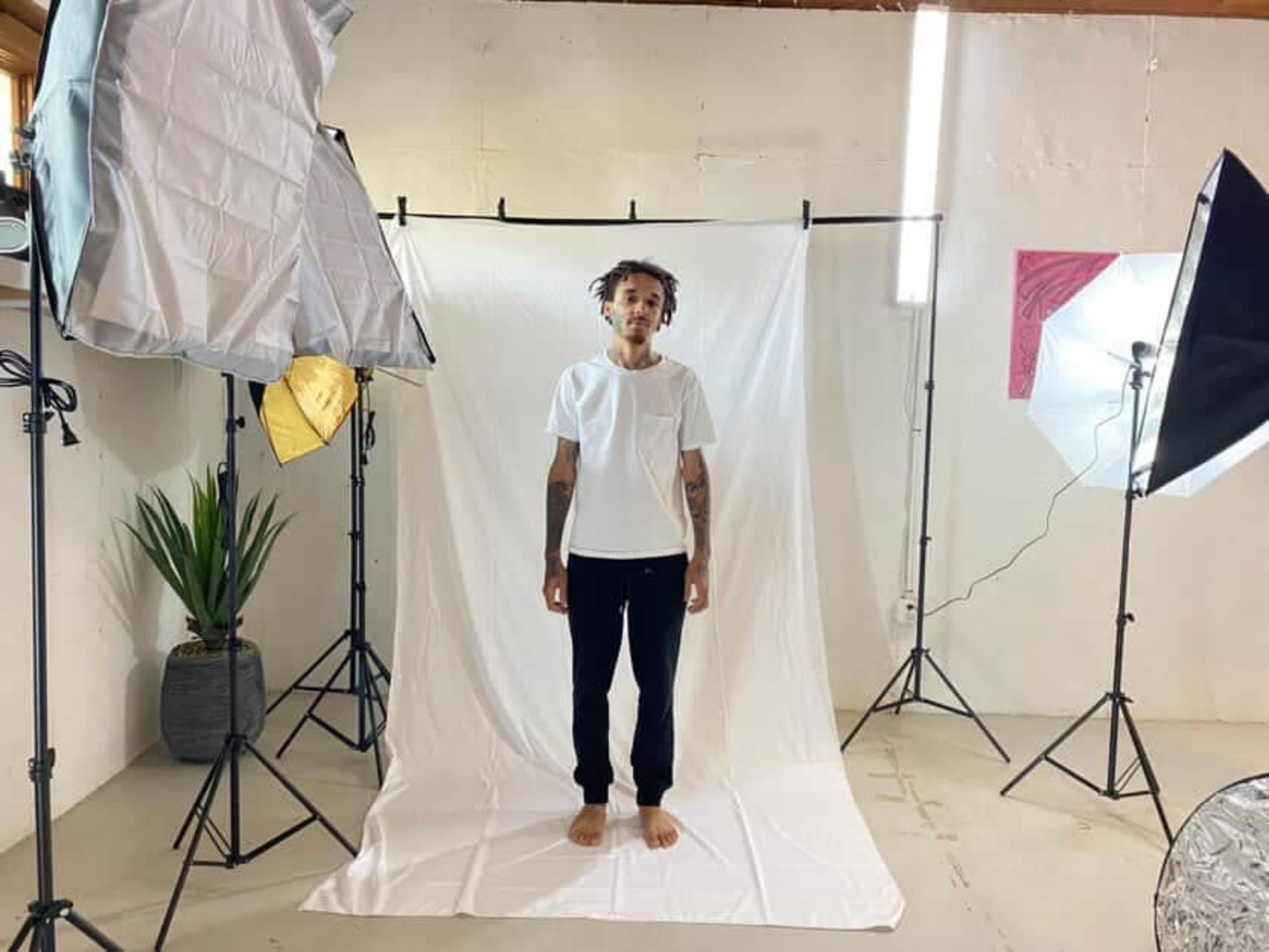 A person stands on a white backdrop surrounded by professional lighting equipment in a studio setting.