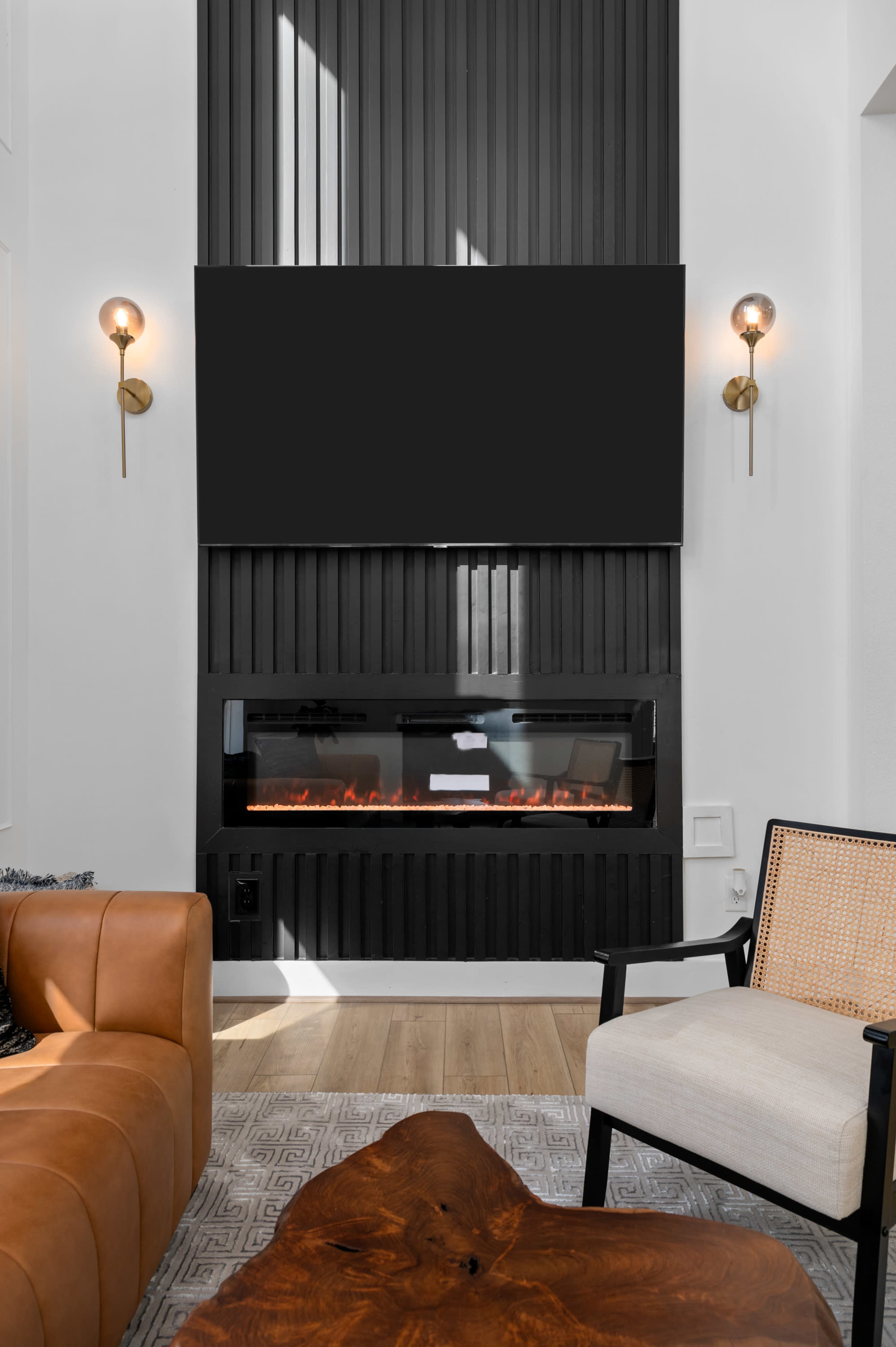 The image features a modern living room with a sleek electric fireplace beneath a wall-mounted television, surrounded by dark paneling and stylish lighting fixtures.