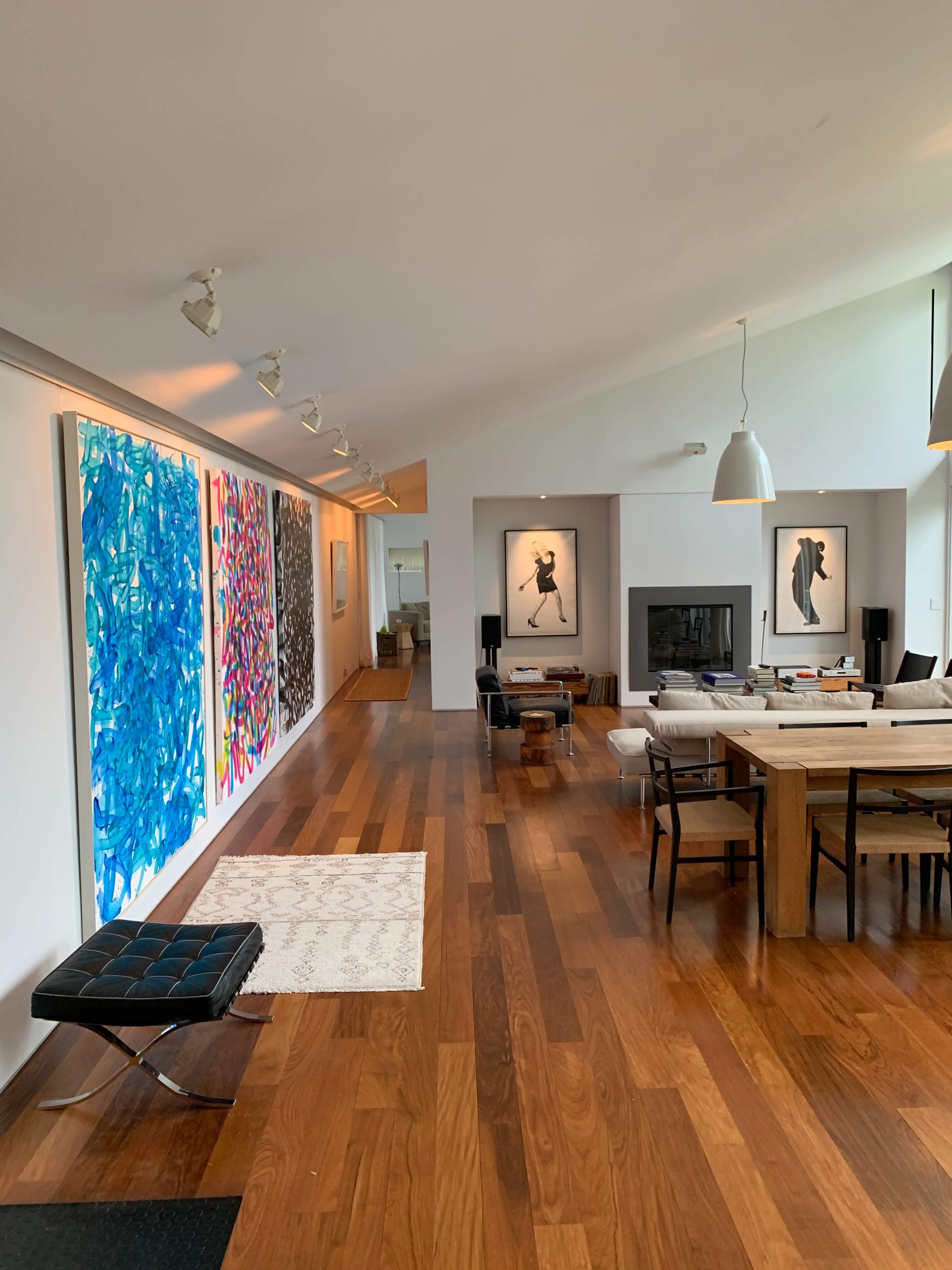 A modern living space features hardwood flooring, artwork on the walls, and a central dining area with a large table and seating arrangements.