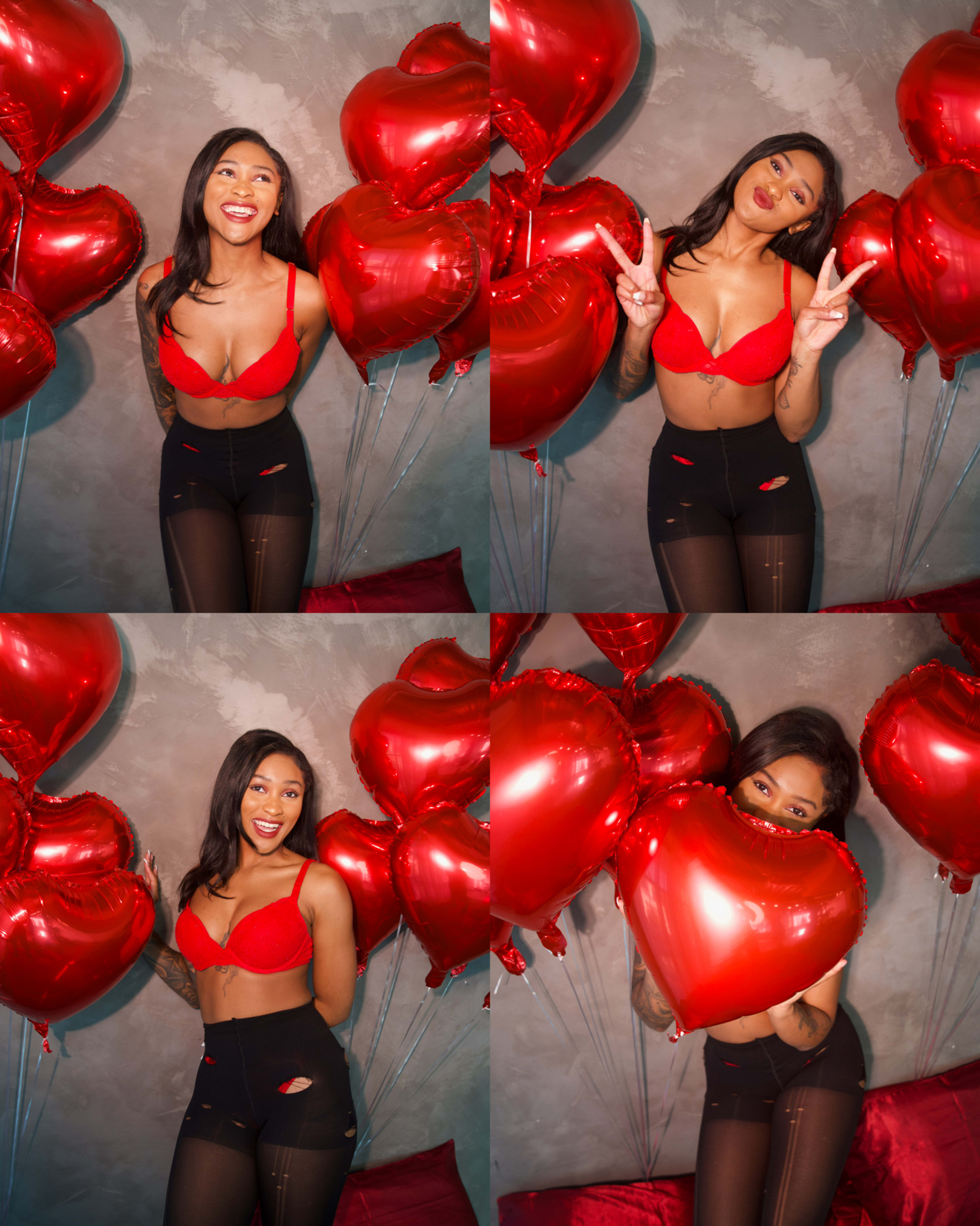 A woman poses playfully with several red heart-shaped balloons in a studio setting.
