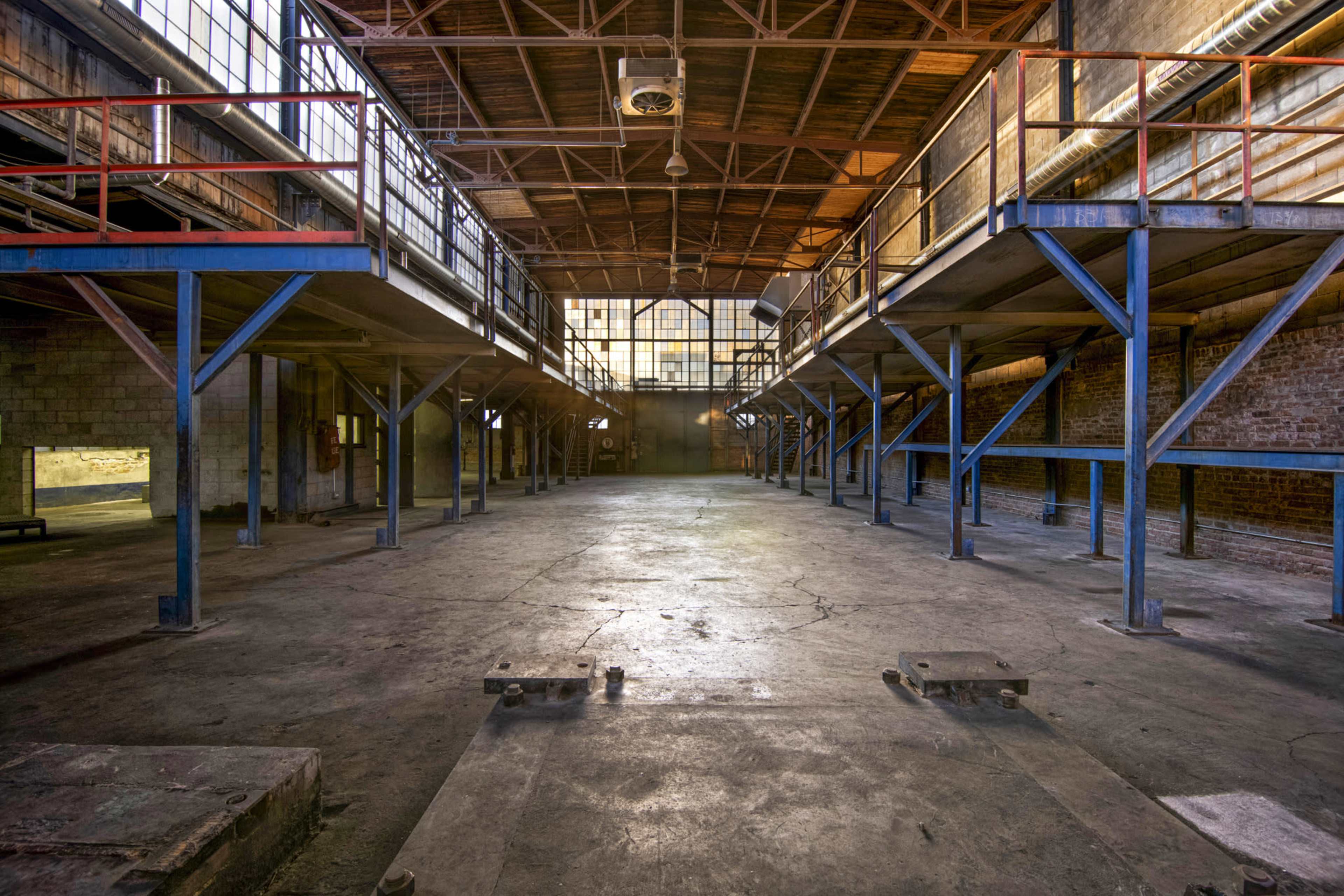 An empty industrial warehouse with elevated platforms and large windows allowing light to enter.