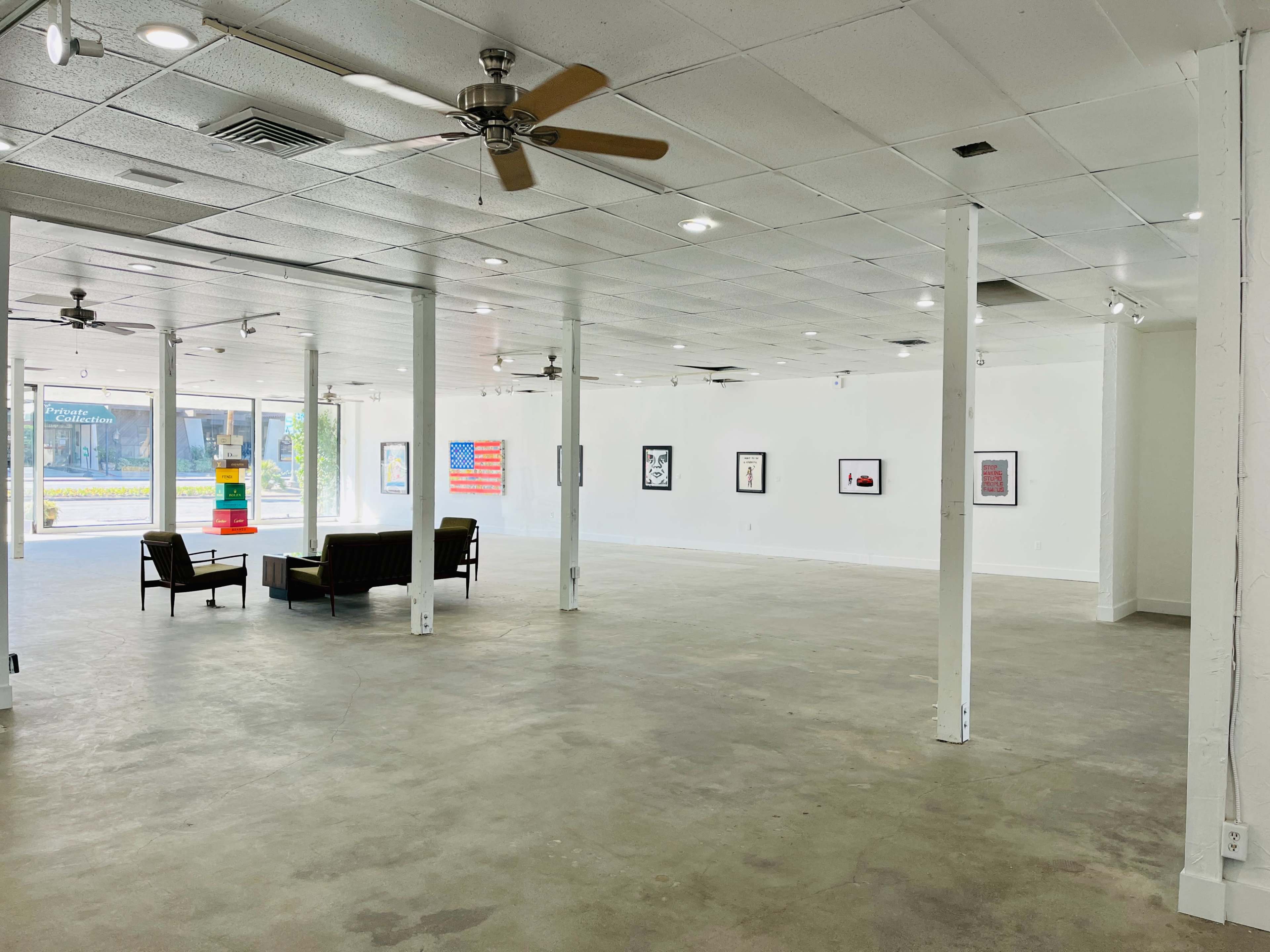 An empty art gallery with white walls, concrete flooring, and a few pieces of framed artwork displayed.