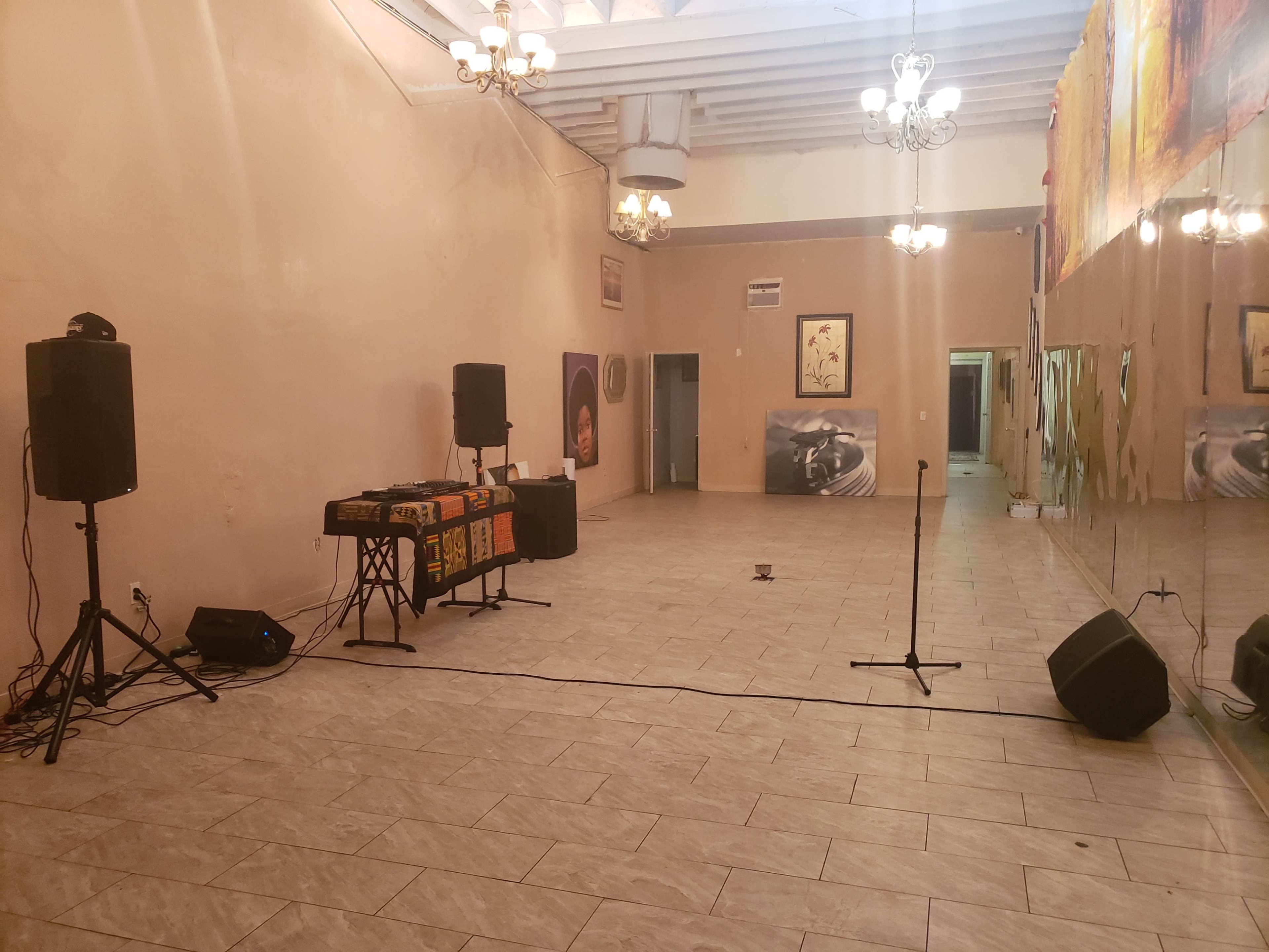 The image shows an empty room with two large speakers, a DJ table, a microphone stand, and mirrors on one wall.