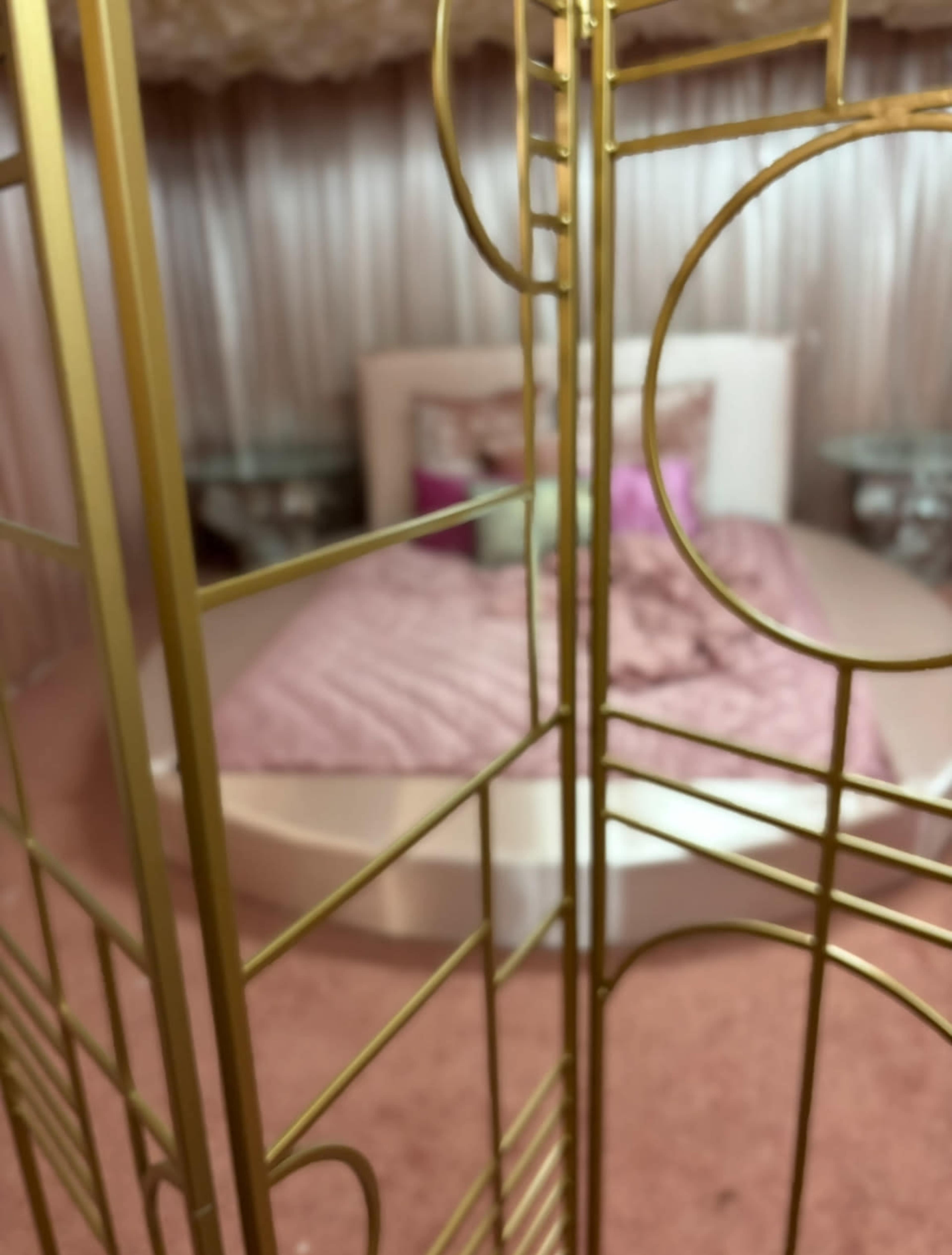 The image shows a glimpse of a circular bed surrounded by decorative gold room dividers and a plush pink carpet.