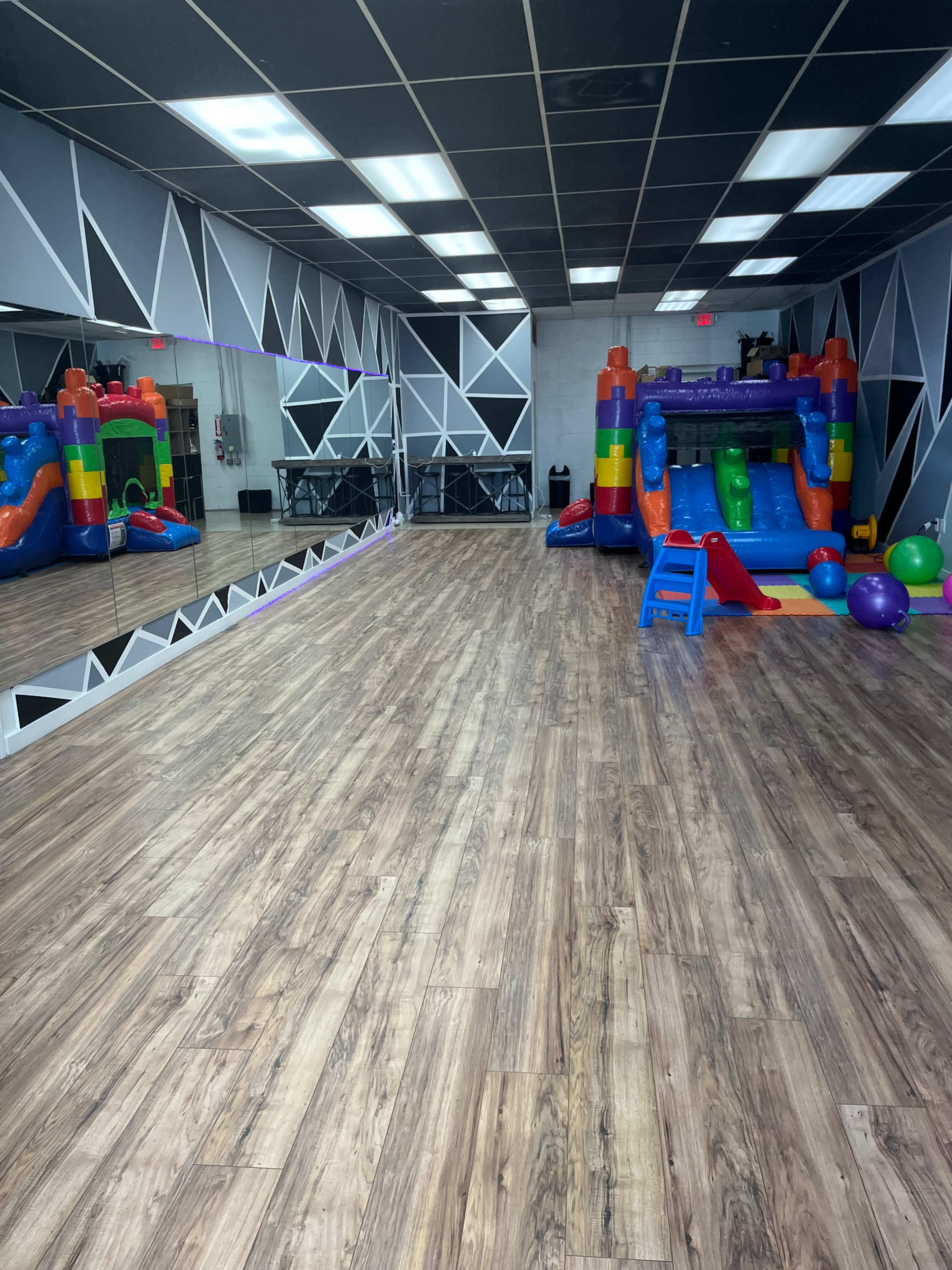An indoor play area featuring a colorful inflatable bounce house on one side and a large mirror along the wall, with wooden flooring throughout.