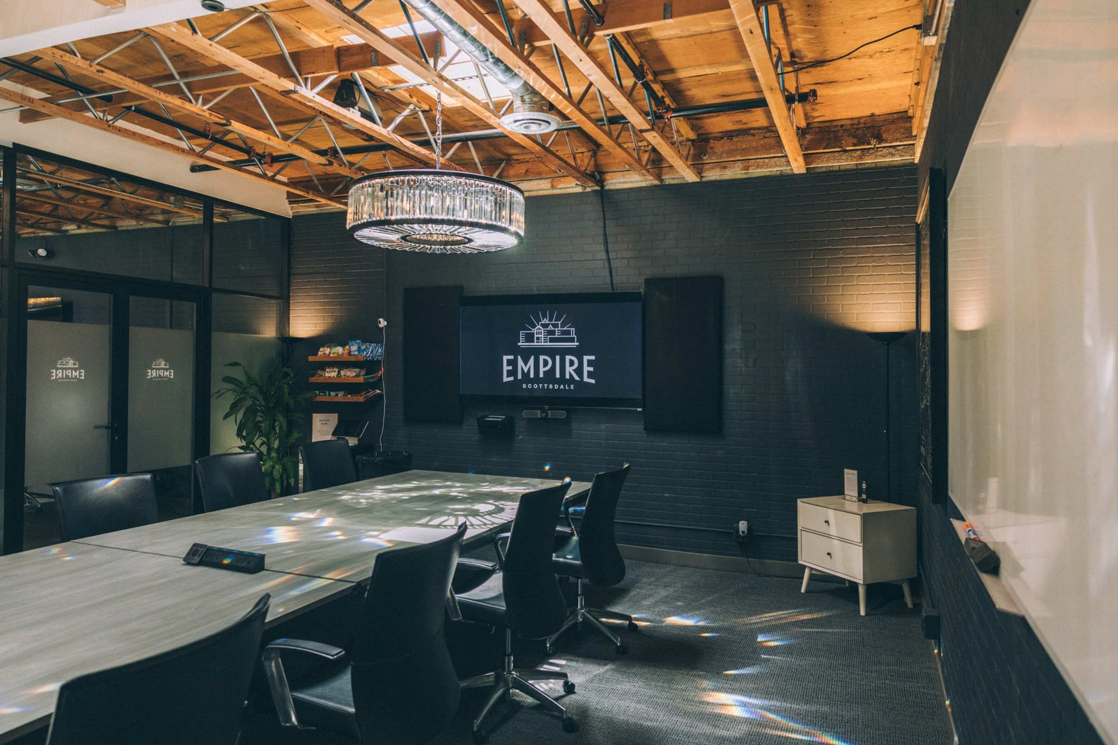 The image shows a modern conference room featuring a large table, black chairs, and a chandelier, with a screen displaying the word "EMPIRE."