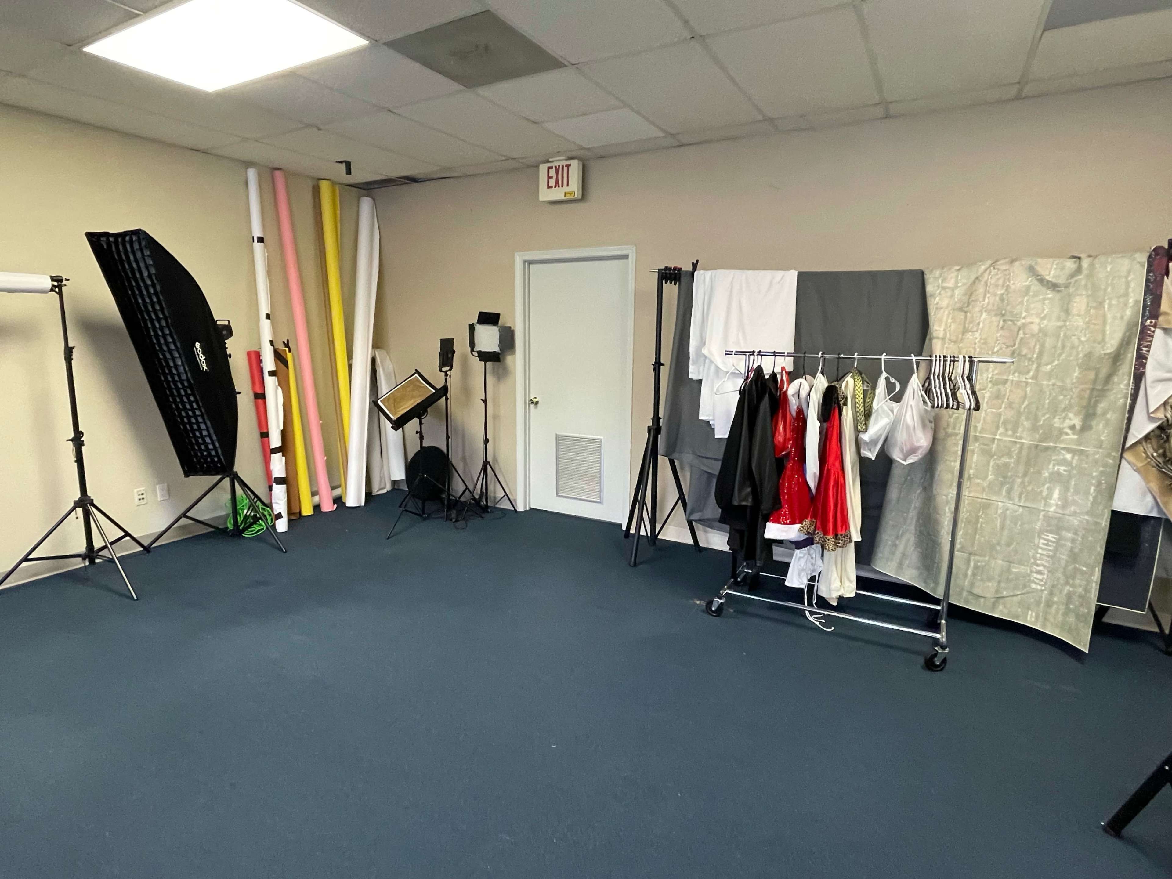 A photography studio with various lighting equipment, backdrops, and a clothing rack.