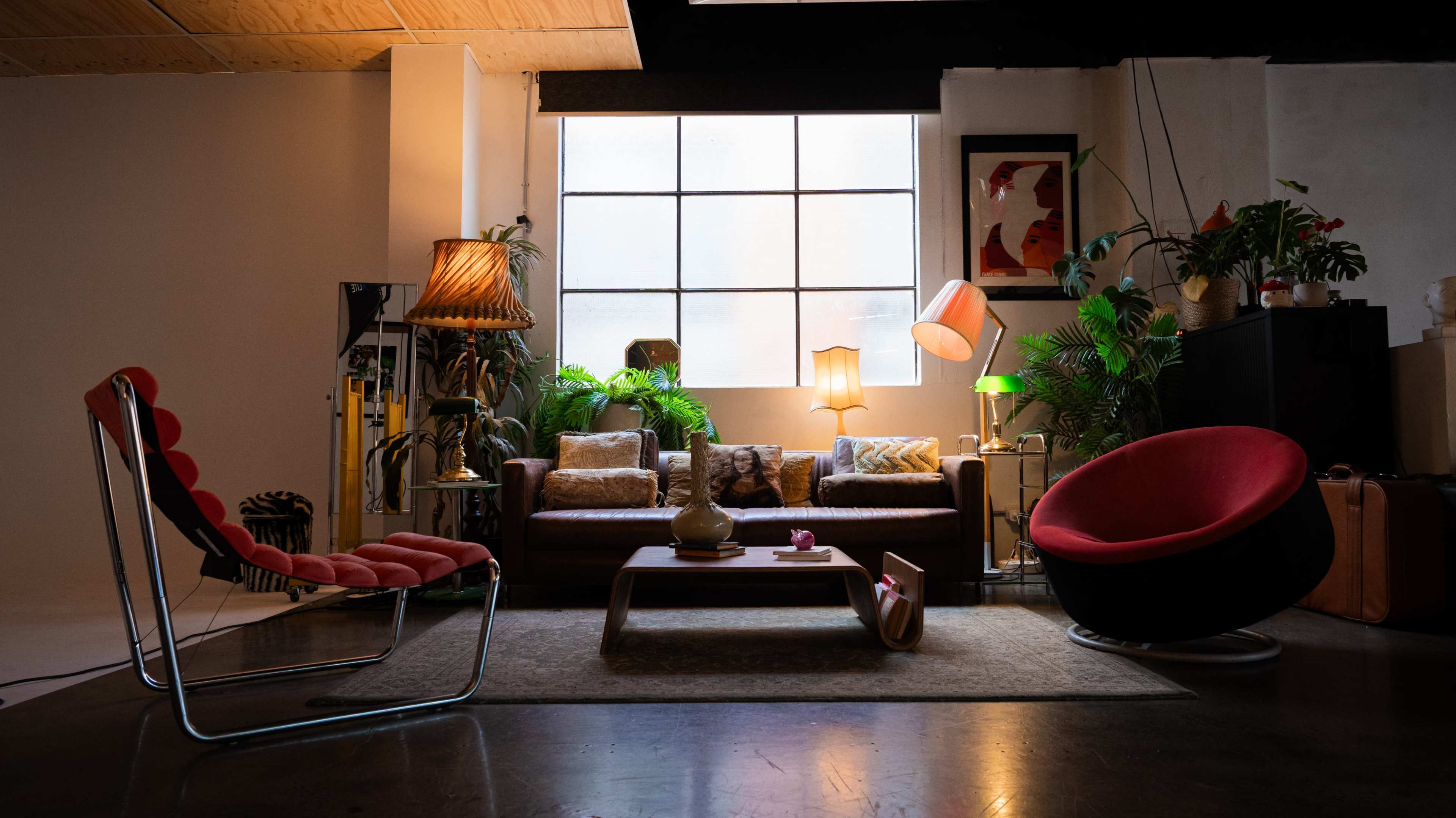 The image shows a cozy and well-decorated living room with a sofa, various armchairs, plants, and multiple lamps.