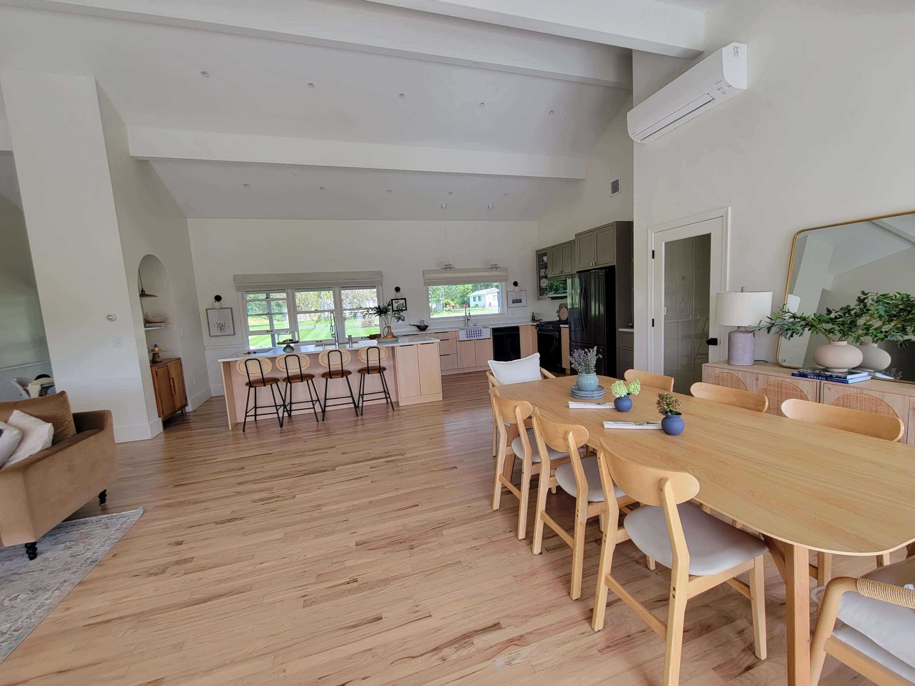 A spacious, open-concept living area featuring a dining table, kitchen island, and seating area with large windows letting in natural light.