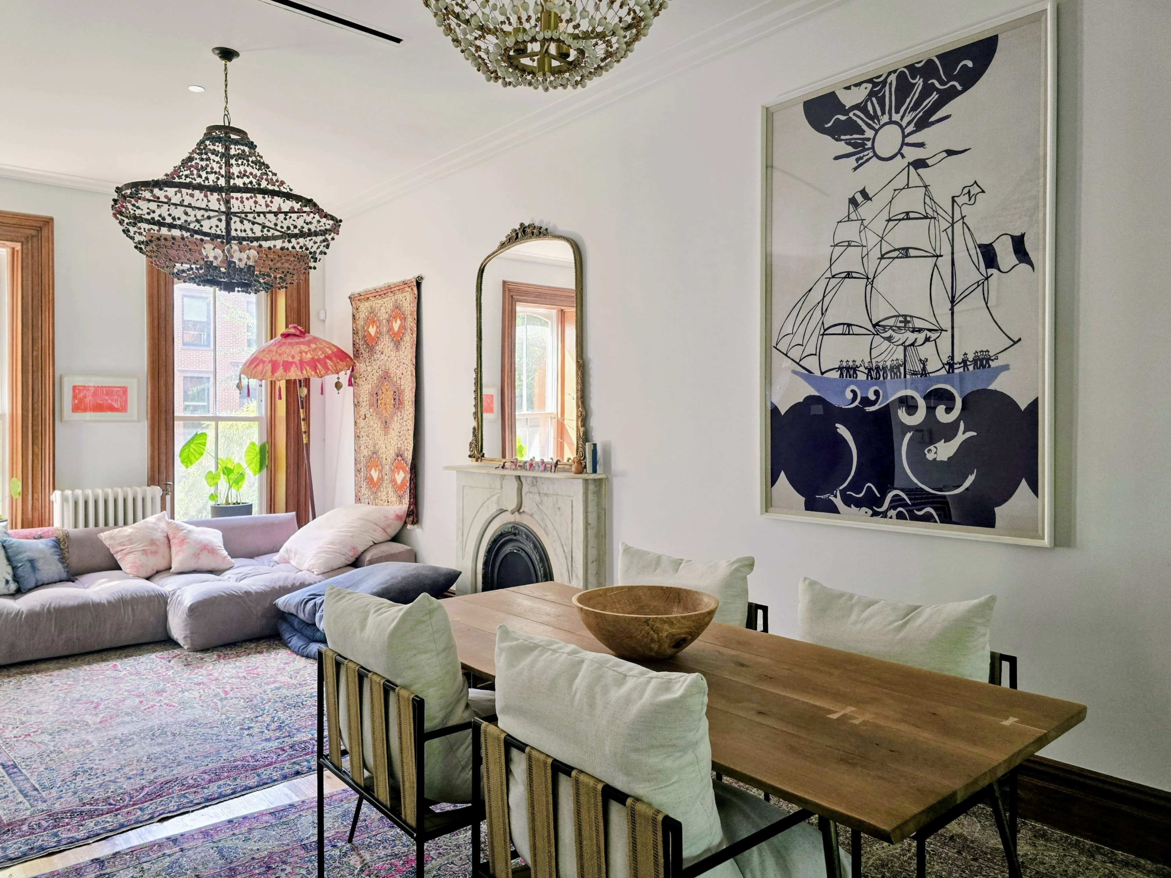 A spacious room features a dining table with chairs, a cozy seating area with large cushions, decorative chandeliers, and artwork on the walls.