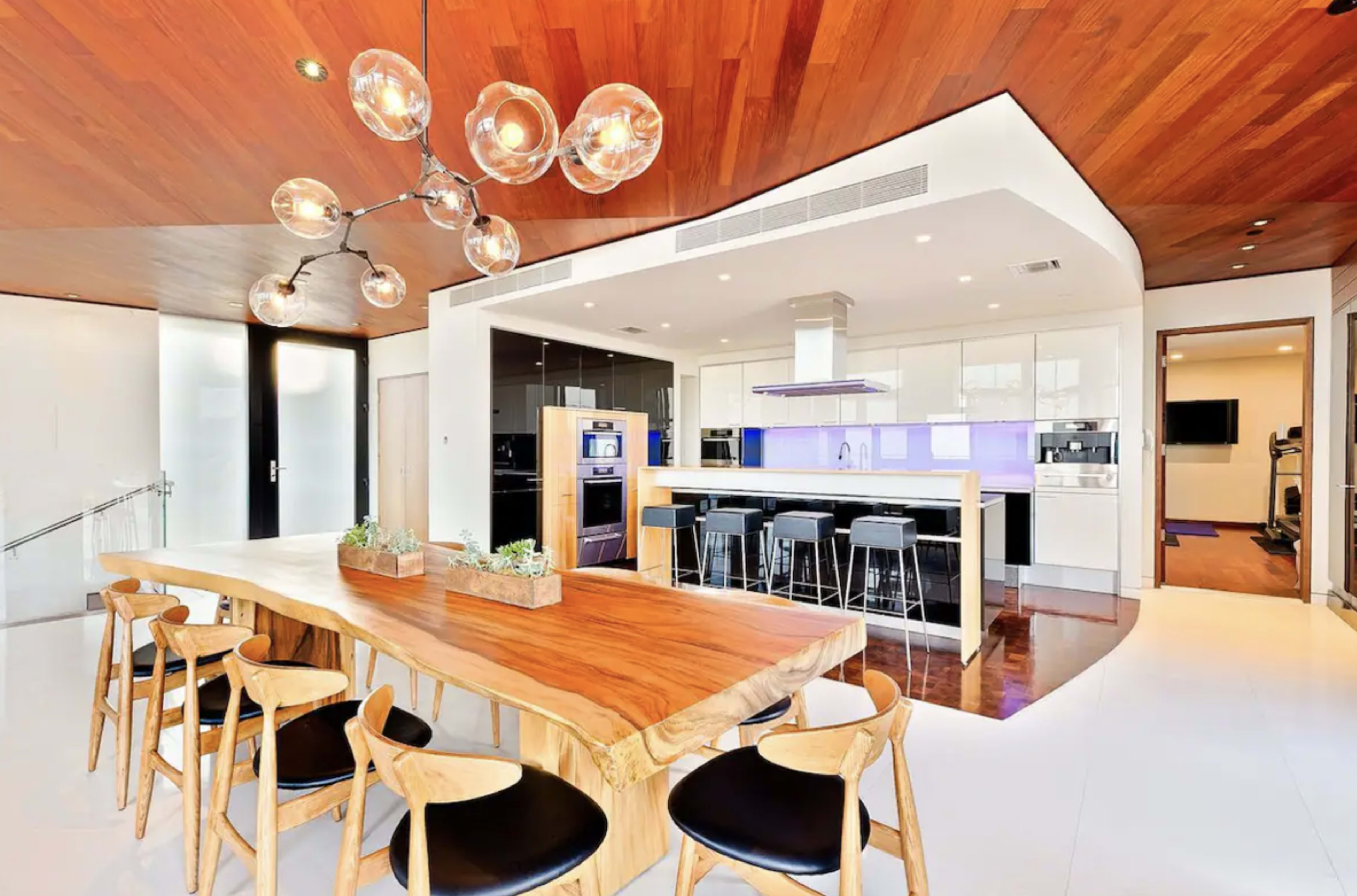 A modern kitchen and dining area with a large wooden table, stylish chairs, and contemporary appliances.