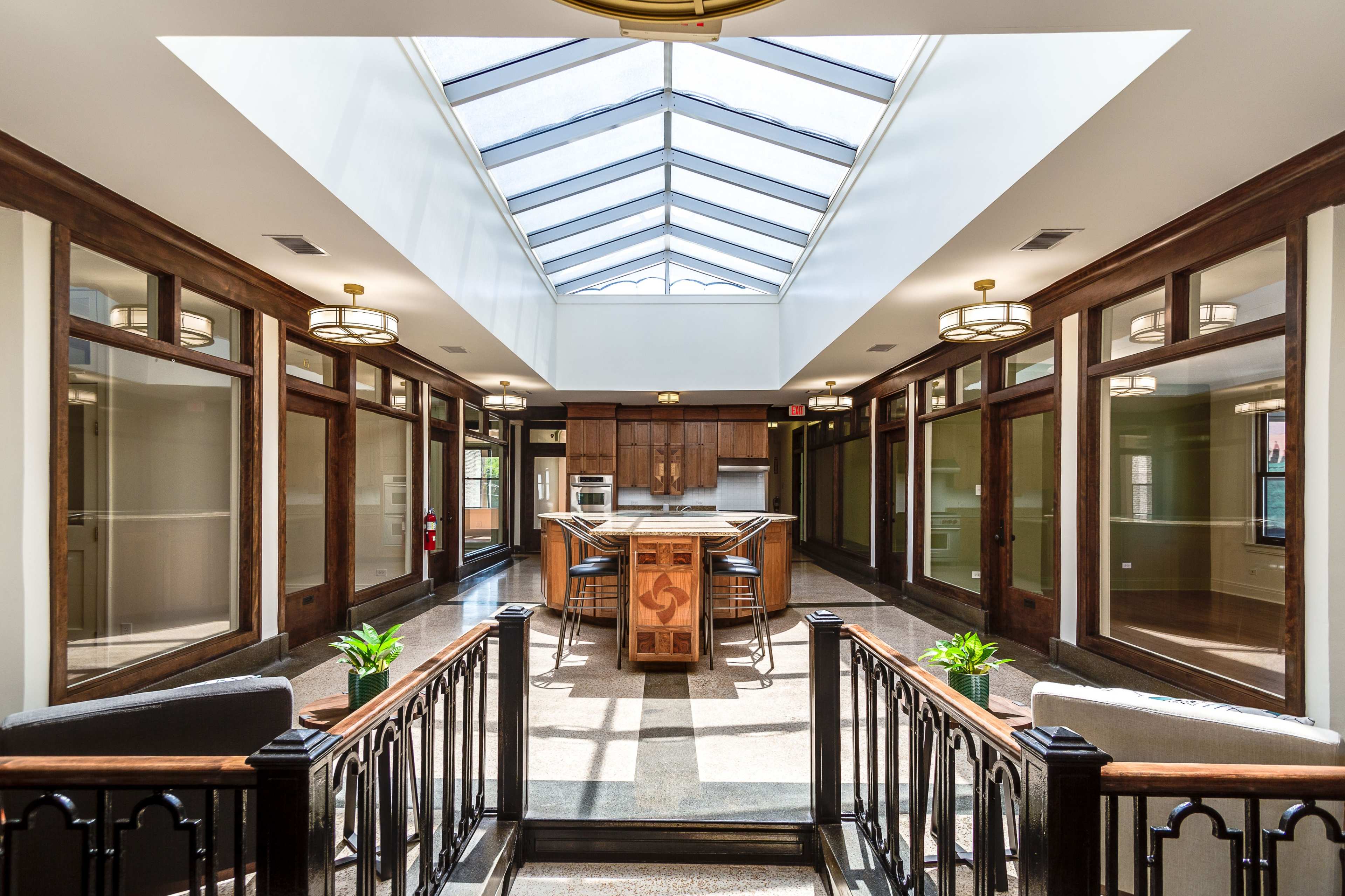 A bright, open kitchen area with a skylight, surrounded by wooden paneling and seating areas, leading to rooms on either side.