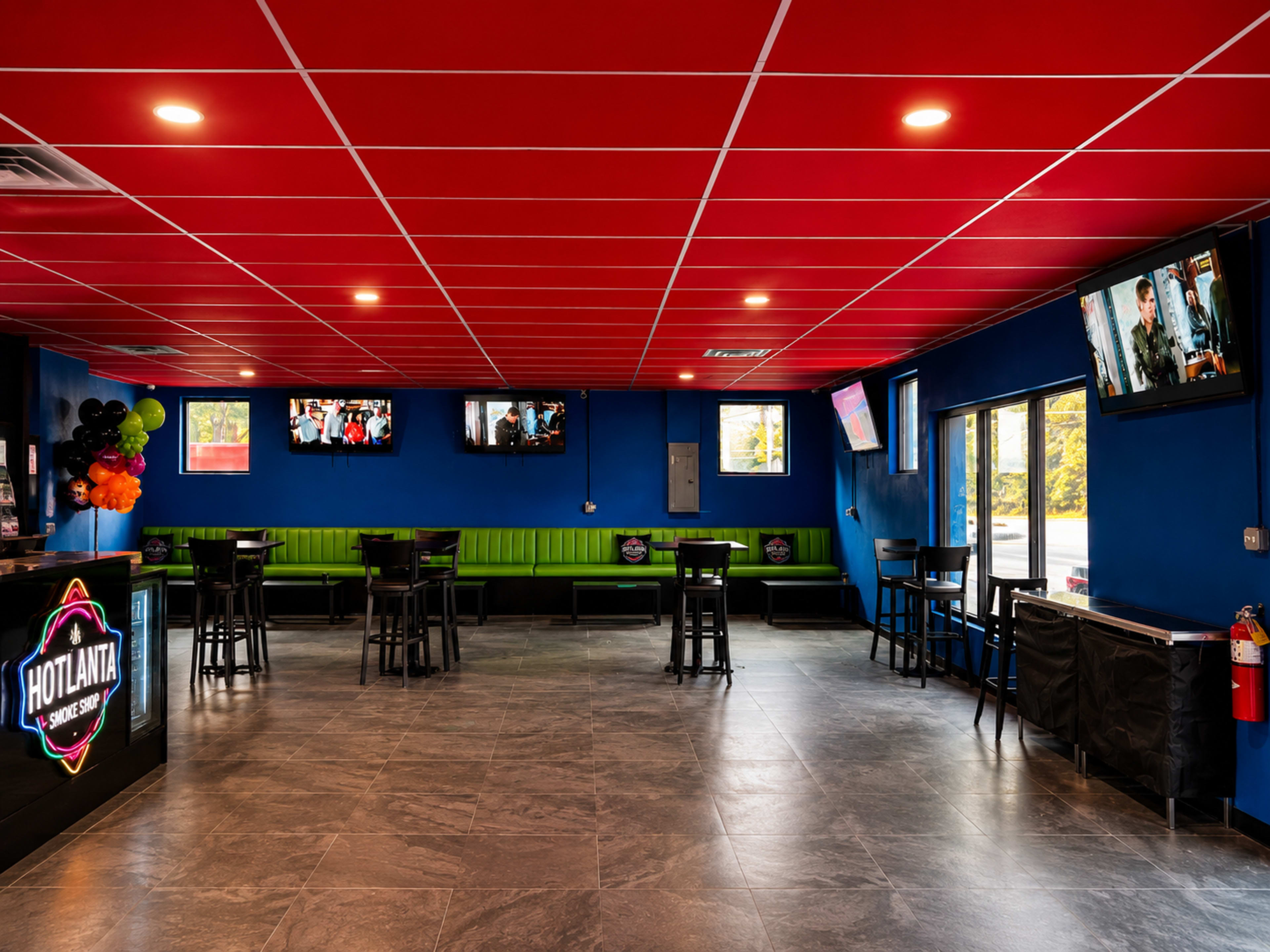 The interior of a sports bar features blue walls, red ceilings, black tables and chairs, and multiple televisions mounted on the walls.