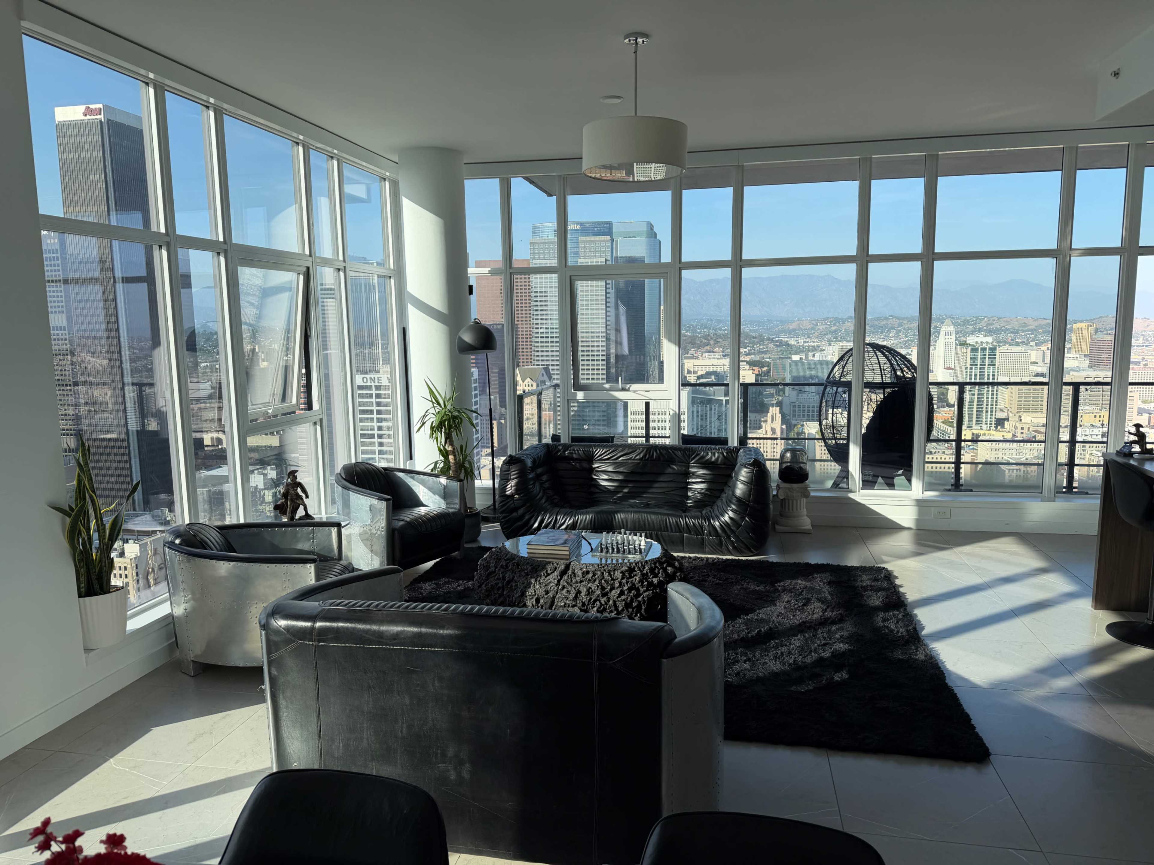 A modern living room features black leather furniture and a large window offering a view of the city skyline.