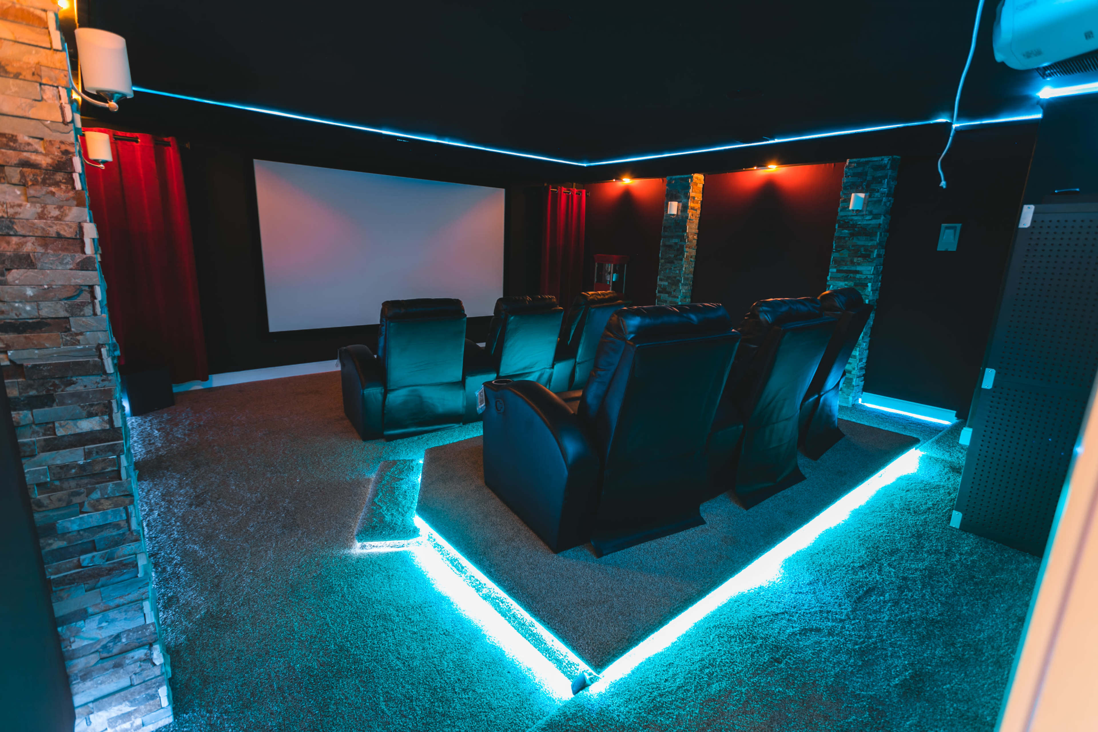 The image shows a home theater room with leather recliners, a large screen, and blue LED lighting along the edges of the carpet.