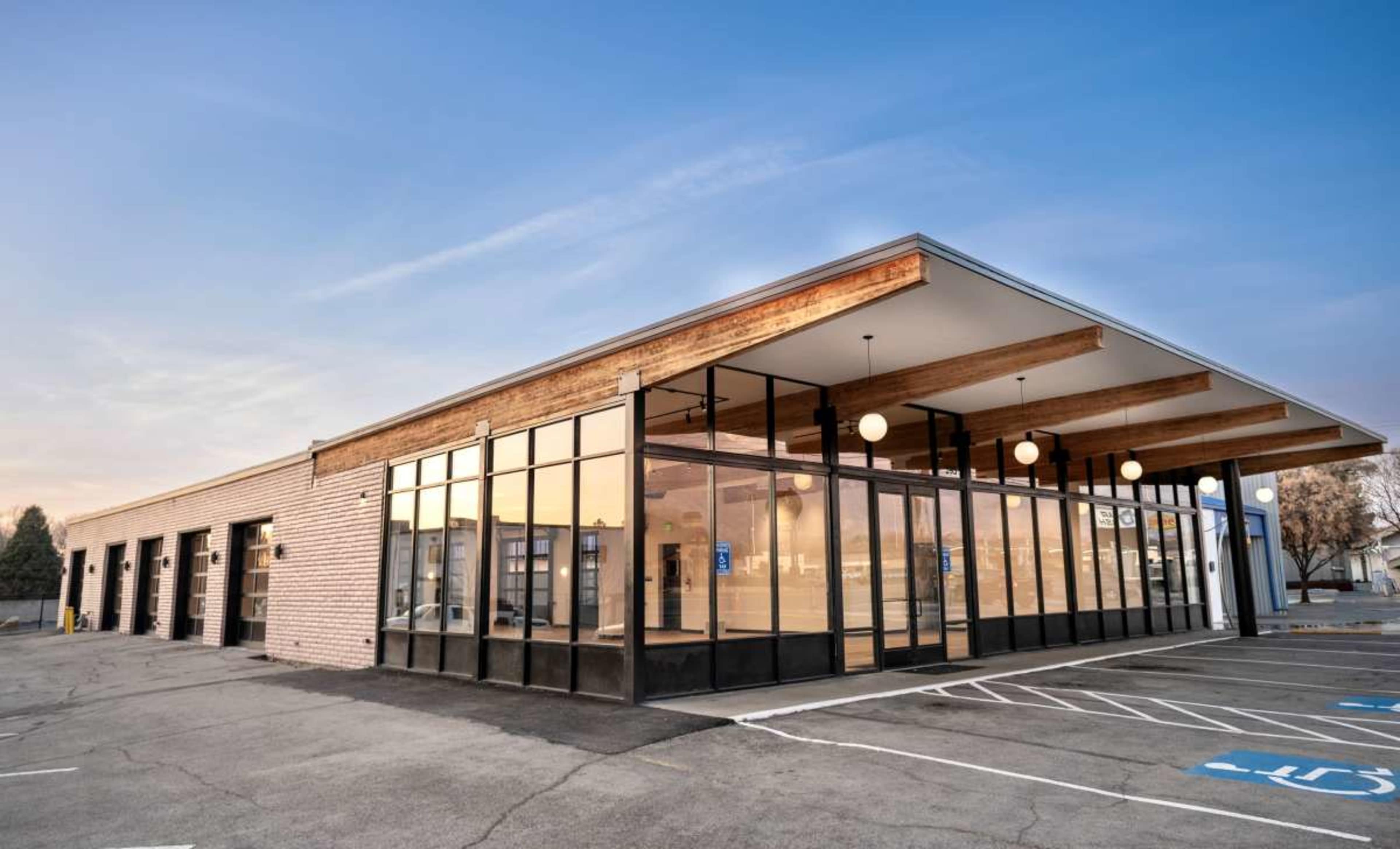 The image shows a modern commercial building with large windows and a distinctive overhang, located in a parking area.